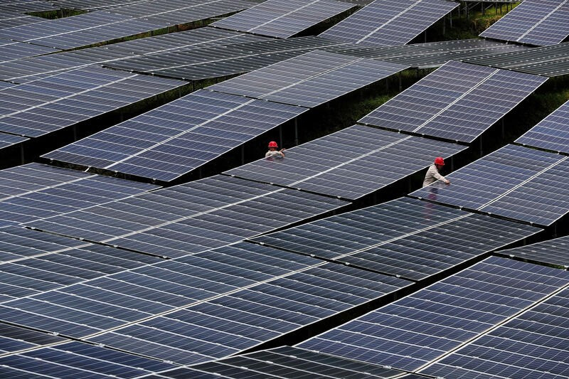 Workers check solar panels at a photovoltaic power station in Chongqing