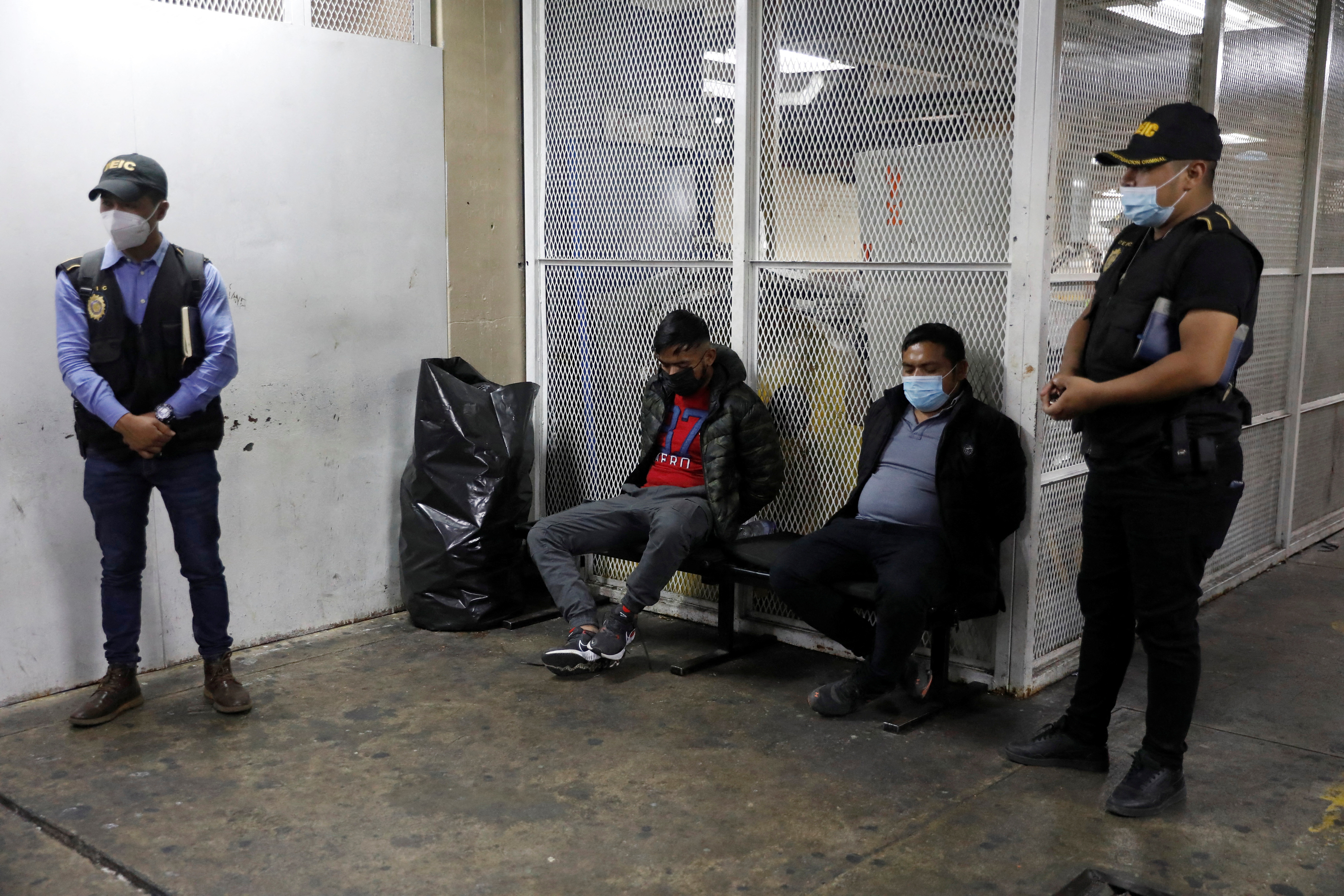 Two detained men sit in the basement of the Supreme Court of Justice in Guatemala City, Guatemala January 28, 2022. An operation by Guatemalan authorities, working with the U.S. Homeland Security agency to arrest people, conducted raids against a migrant smuggling group linked to the massacre of 19 people in Mexico last year. REUTERS/Luis Echeverria