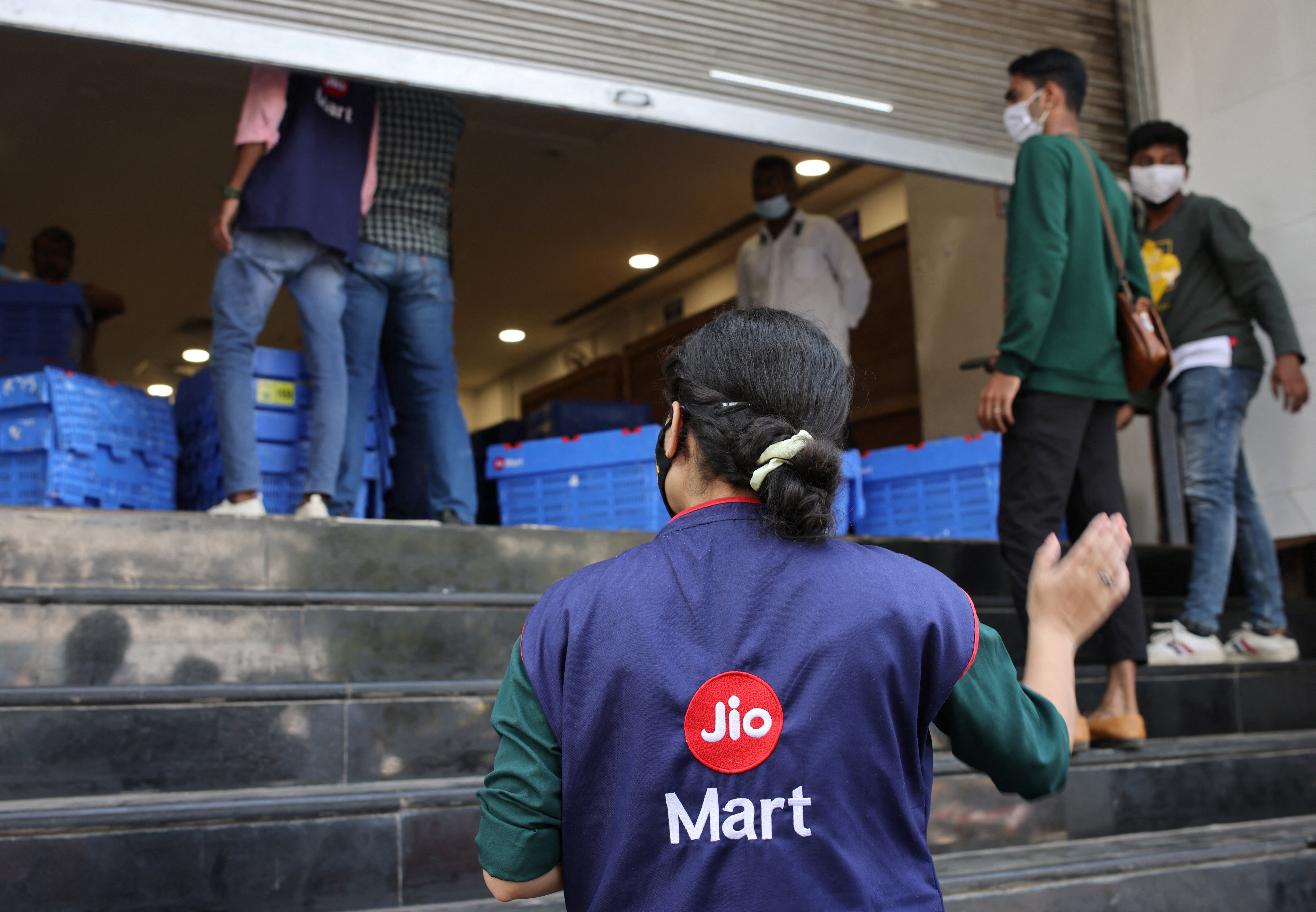 A woman wearing a Reliance JioMart vest instructs workers as they stock their products inside a Future Retail's closed Big Bazaar retail store in Mumbai