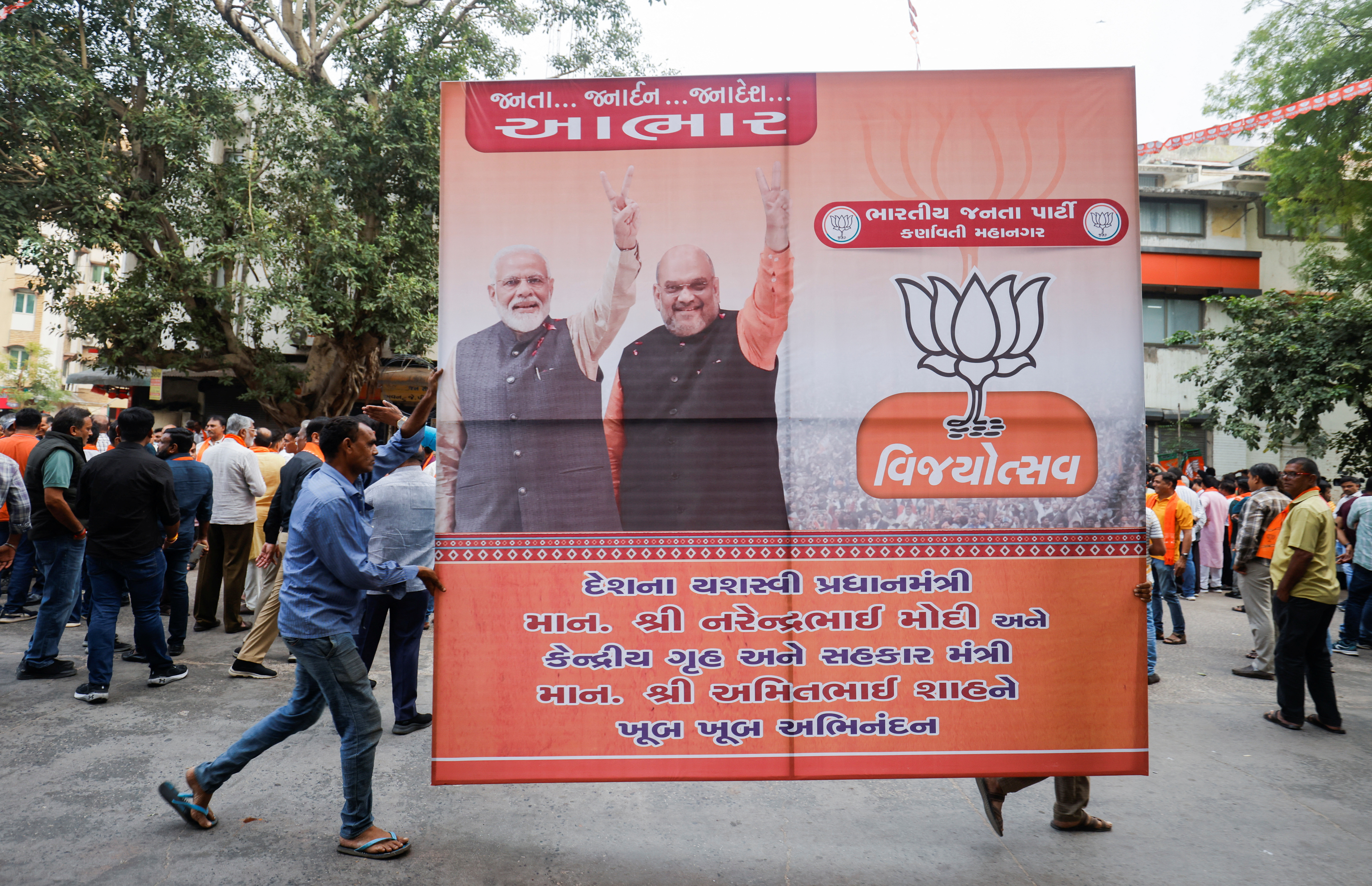Supporters of India's ruling Bharatiya Janata Party (BJP) carry a hoarding of Indian Prime Minister Narendra Modi and Union Minister of Home Affairs Amit Shah for celebrations in Ahmedabad