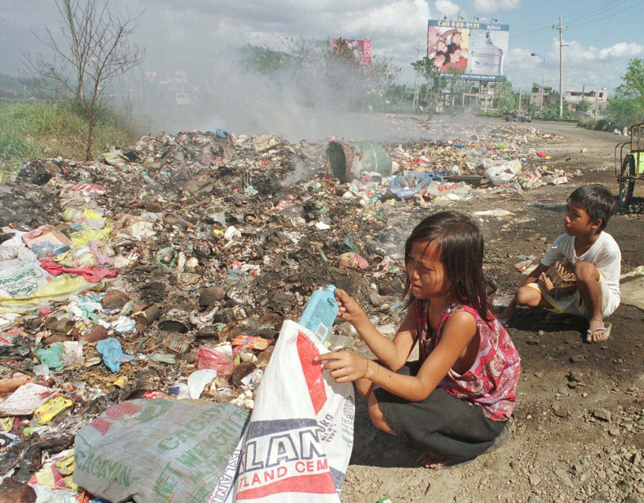 Filipino children gather scraps and other recyclable materials from a smoking garbage dump in Manila