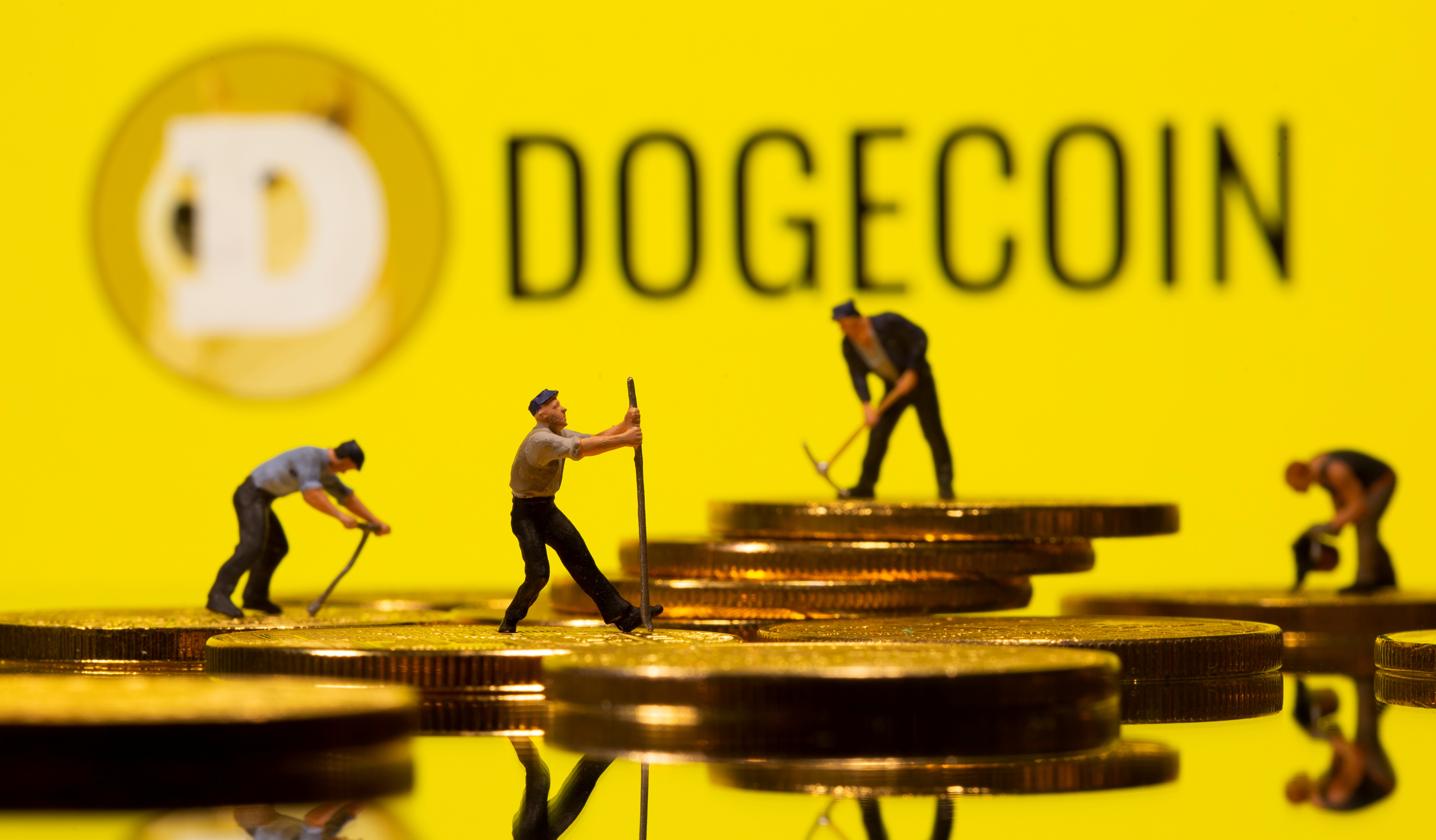 Small toy figures are seen on the cryptocurrency representation with Dogecoin logo in the background in this illustration