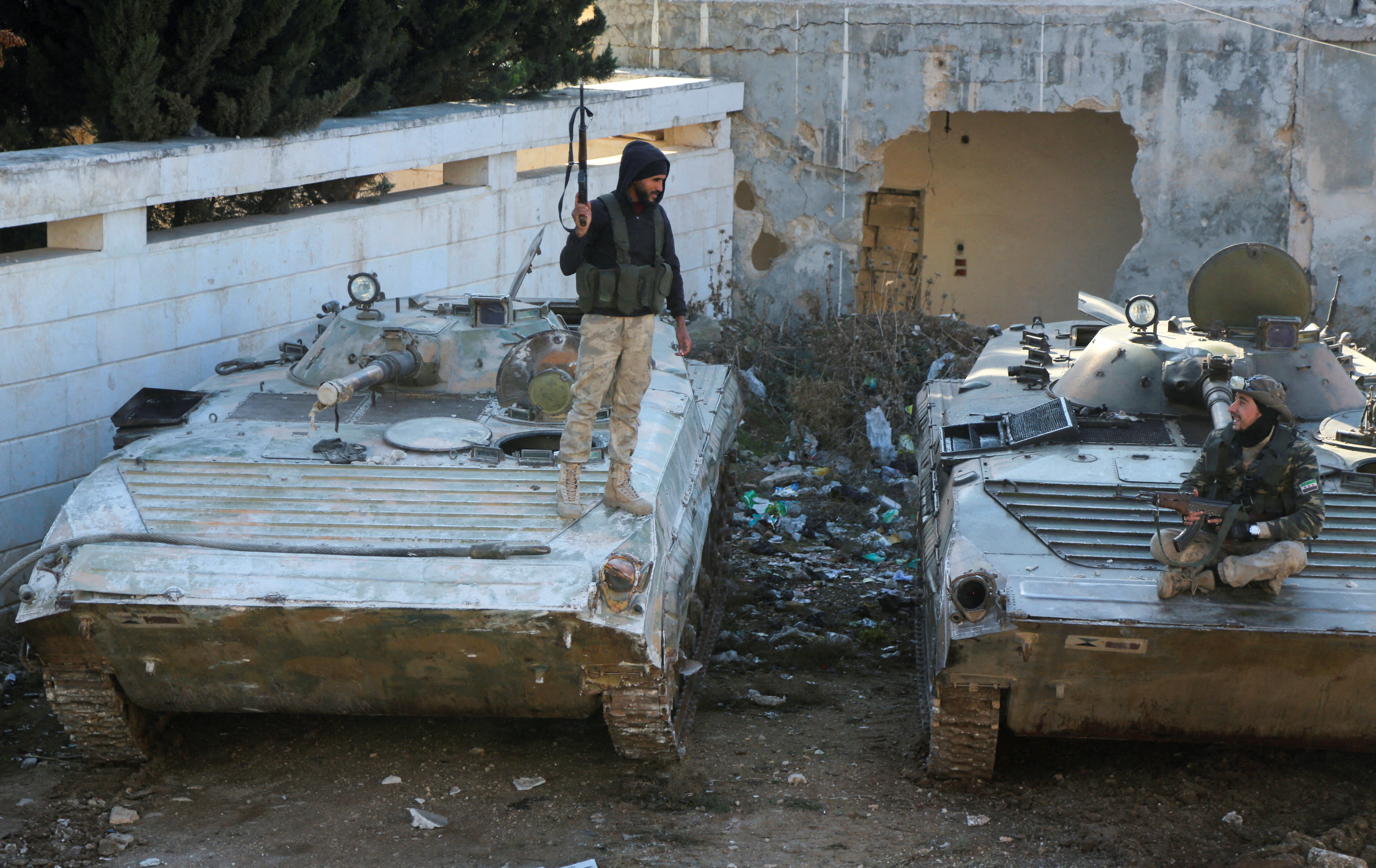 Rebel fighters talk together as one of them stands on a military vehicle holding a weapon in the town of Tel Rifaat