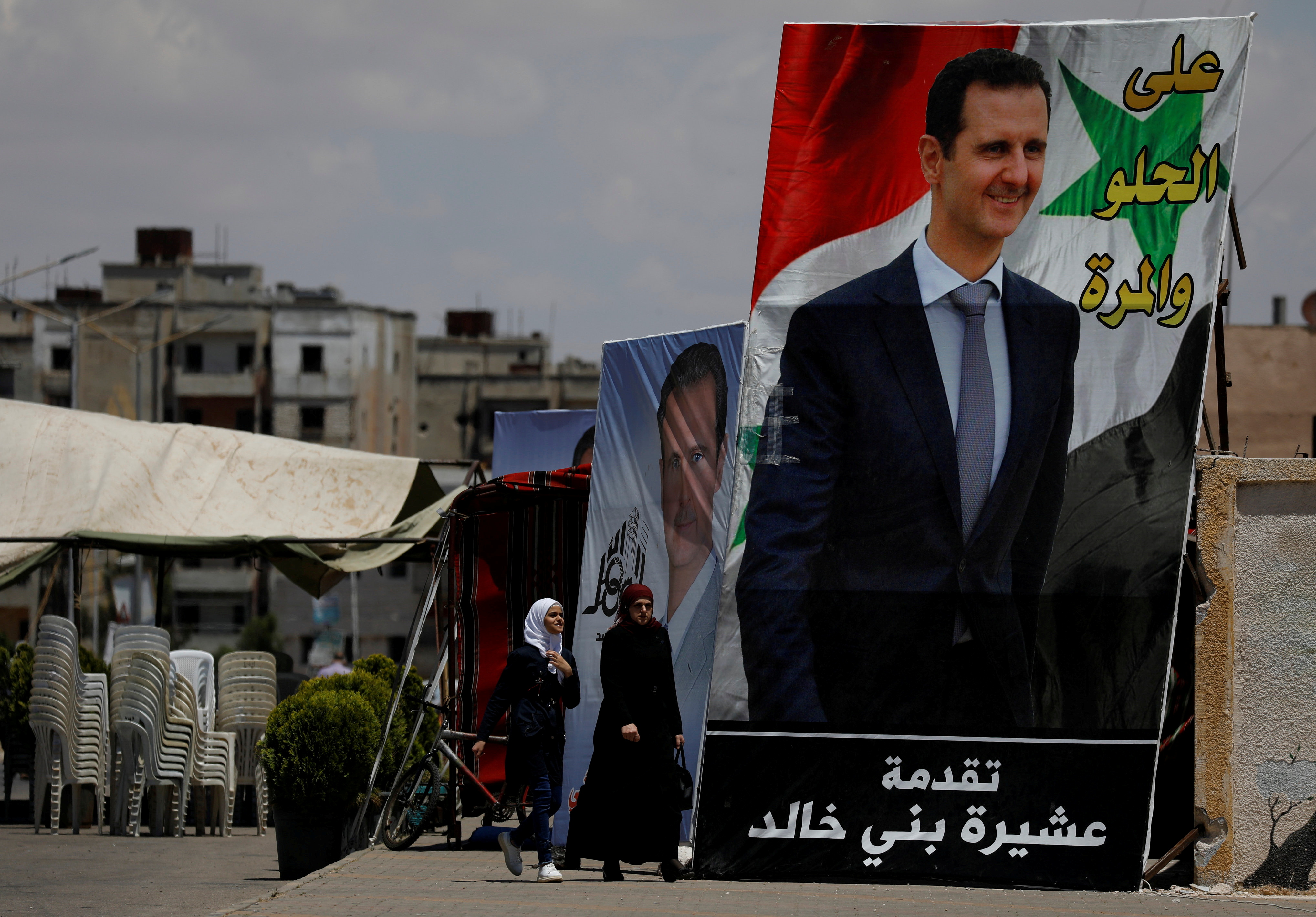 People walk past posters depciting Syria's President Bashar al-Assad, ahead of the May 26 presidential election, in the district of al-Waer in Homs, Syria May 23, 2021.  Picture taken May 23, 2021. REUTERS/Omar Sanadiki/File Photo