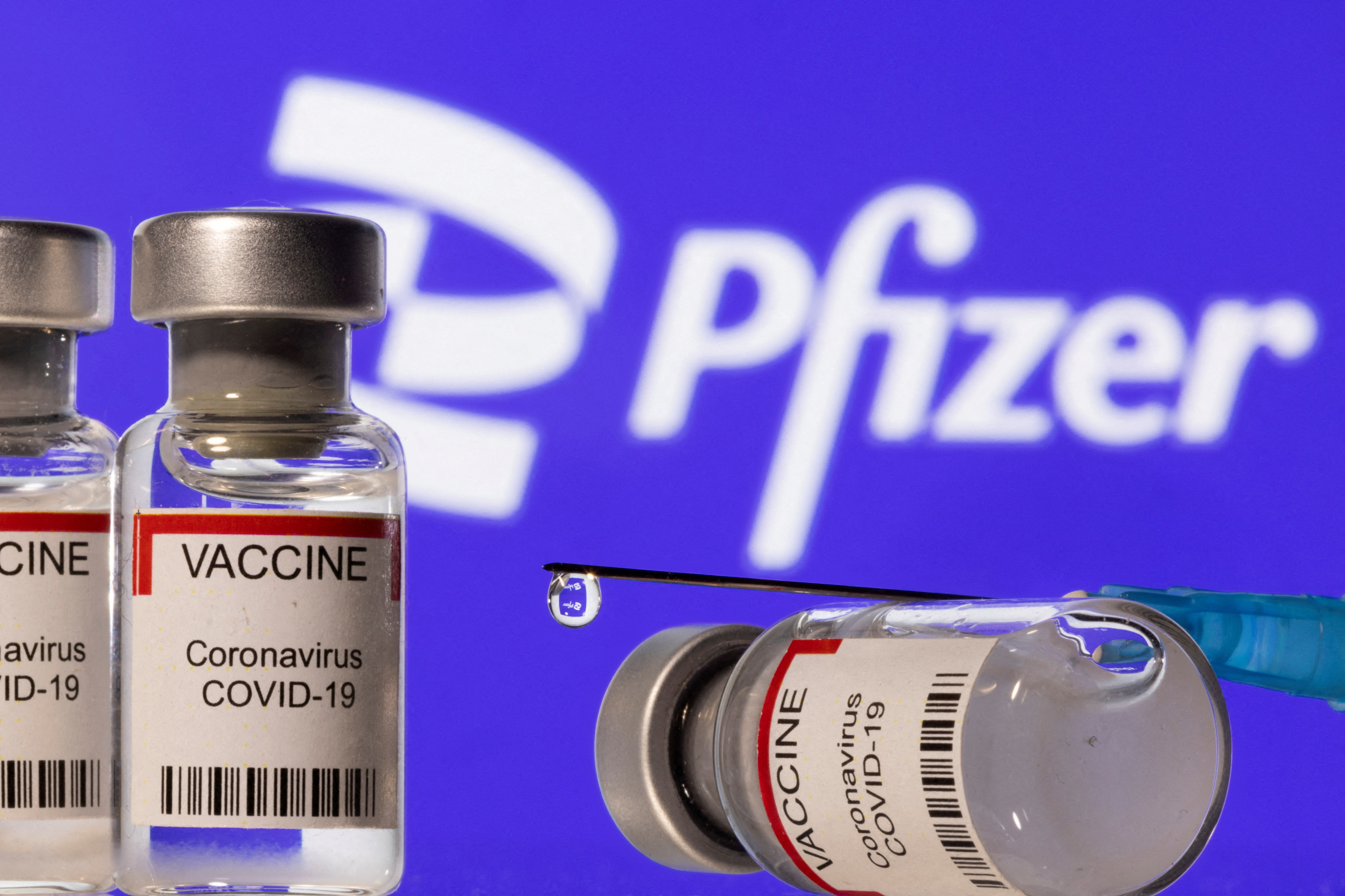 Illustration shows vials labelled "VACCINE Coronavirus COVID-19" and a syringe in front of a displayed Pfizer logo