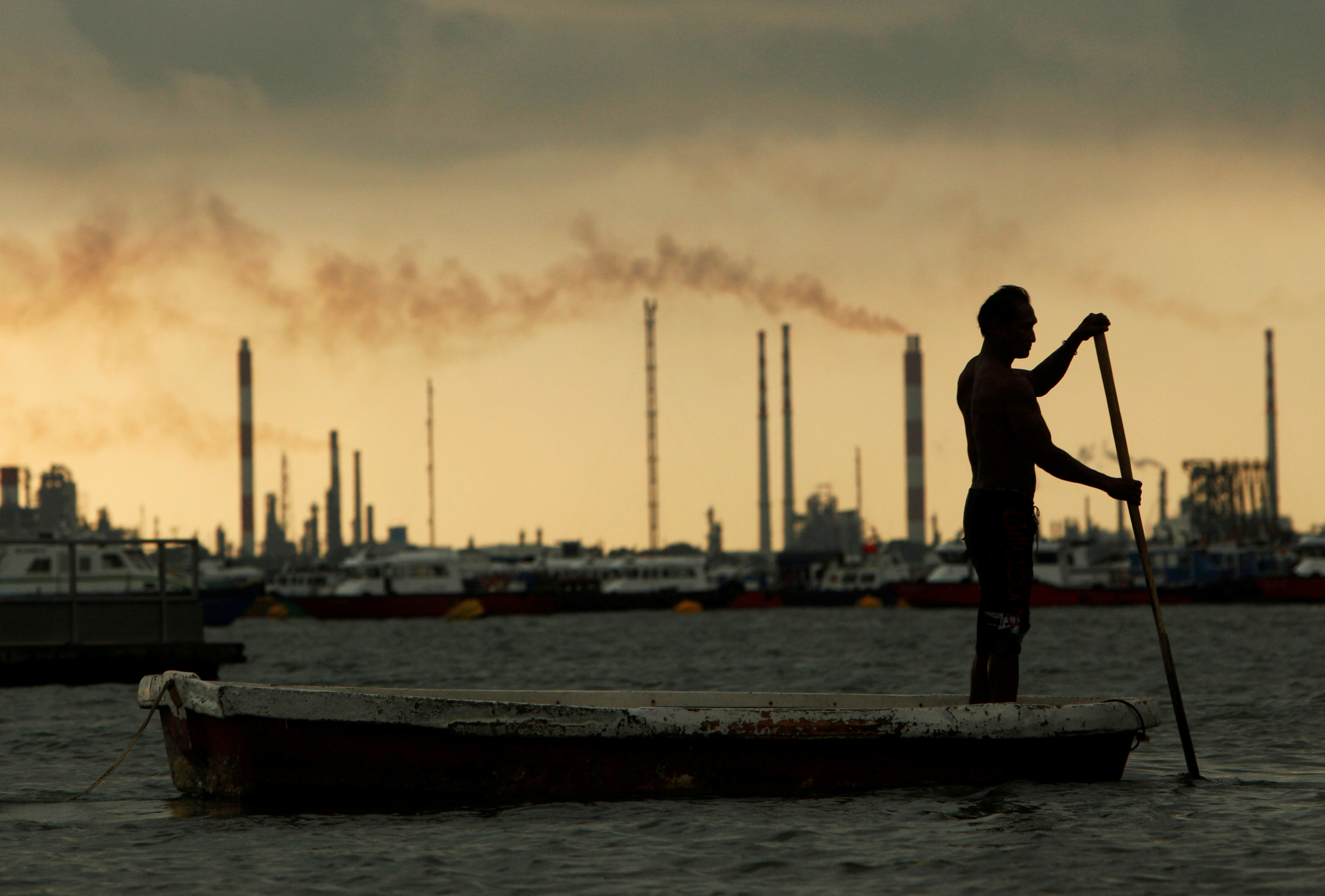 A fisherman rows his dinghy past oil refineries near port terminals in Singapore