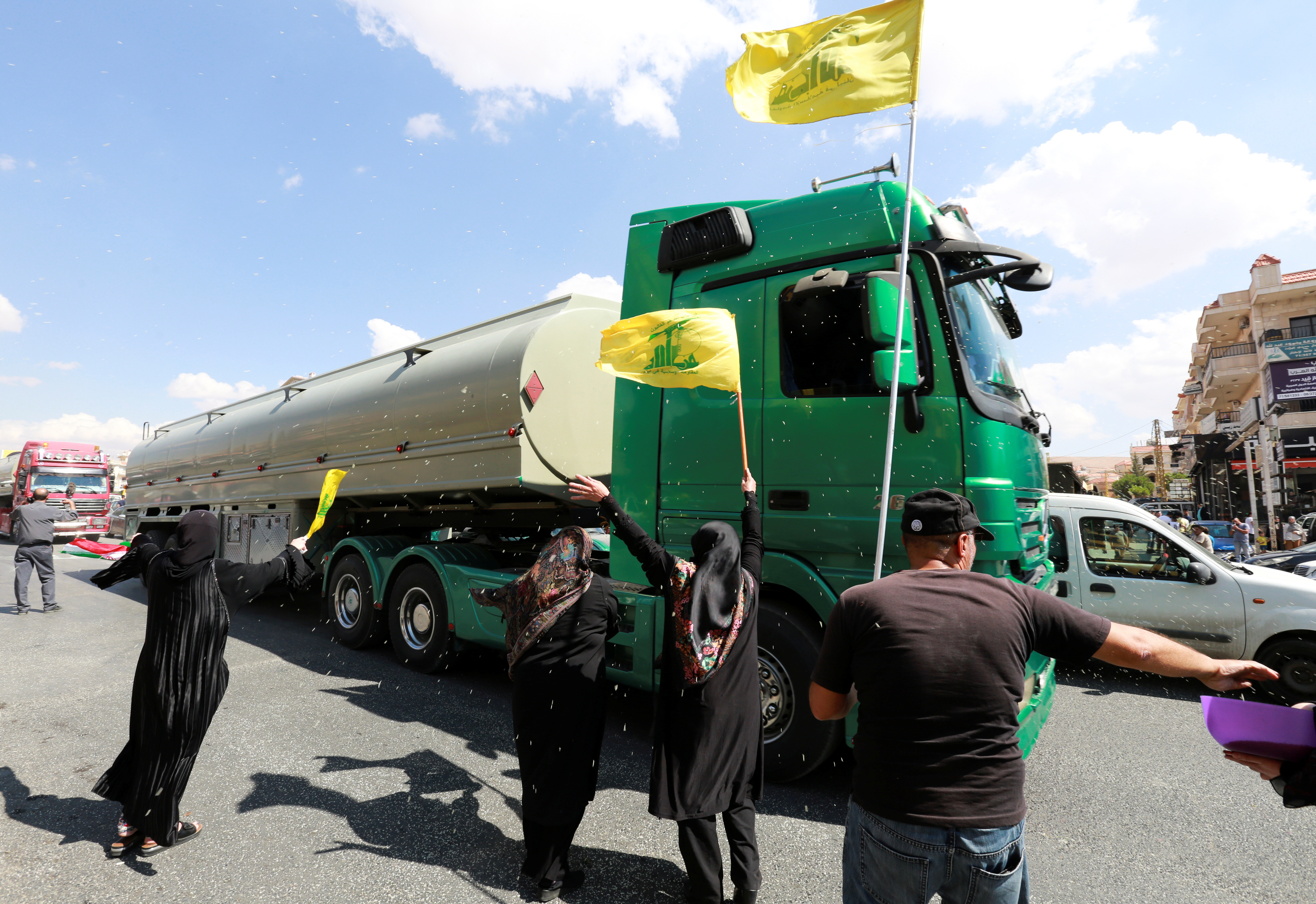 Women hold Hezbollah flags as a convoy of tanker trucks carrying Iranian fuel oil drive in Baalbeck