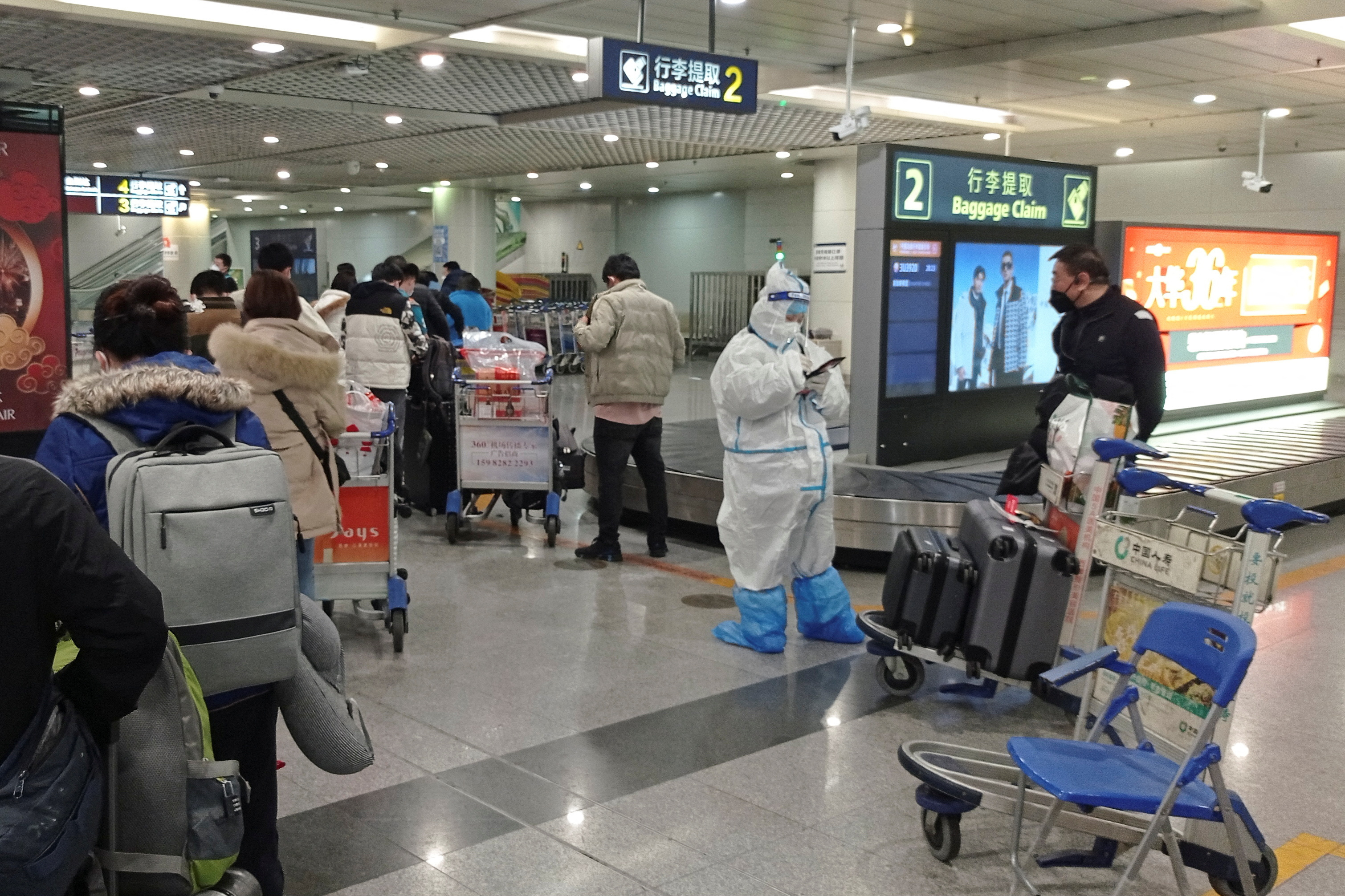 Passengers arriving on international flights wait in line next to a staff member wearing personal protective equipment (PPE) at the airport in Chengdu