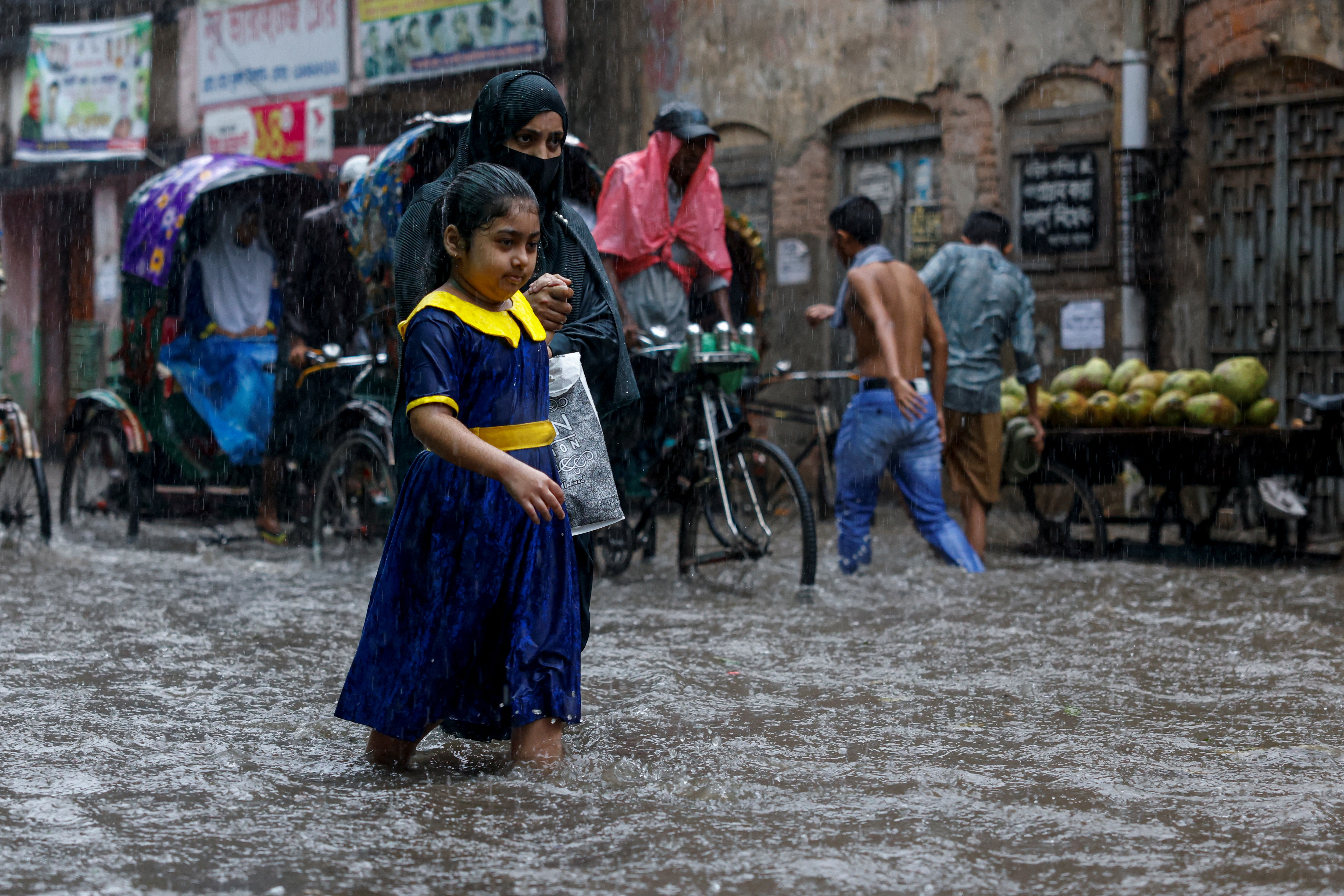 A woman helps a schoolgirl while walking along a flooded street on their way back home after school, during heavy rain in Dhaka