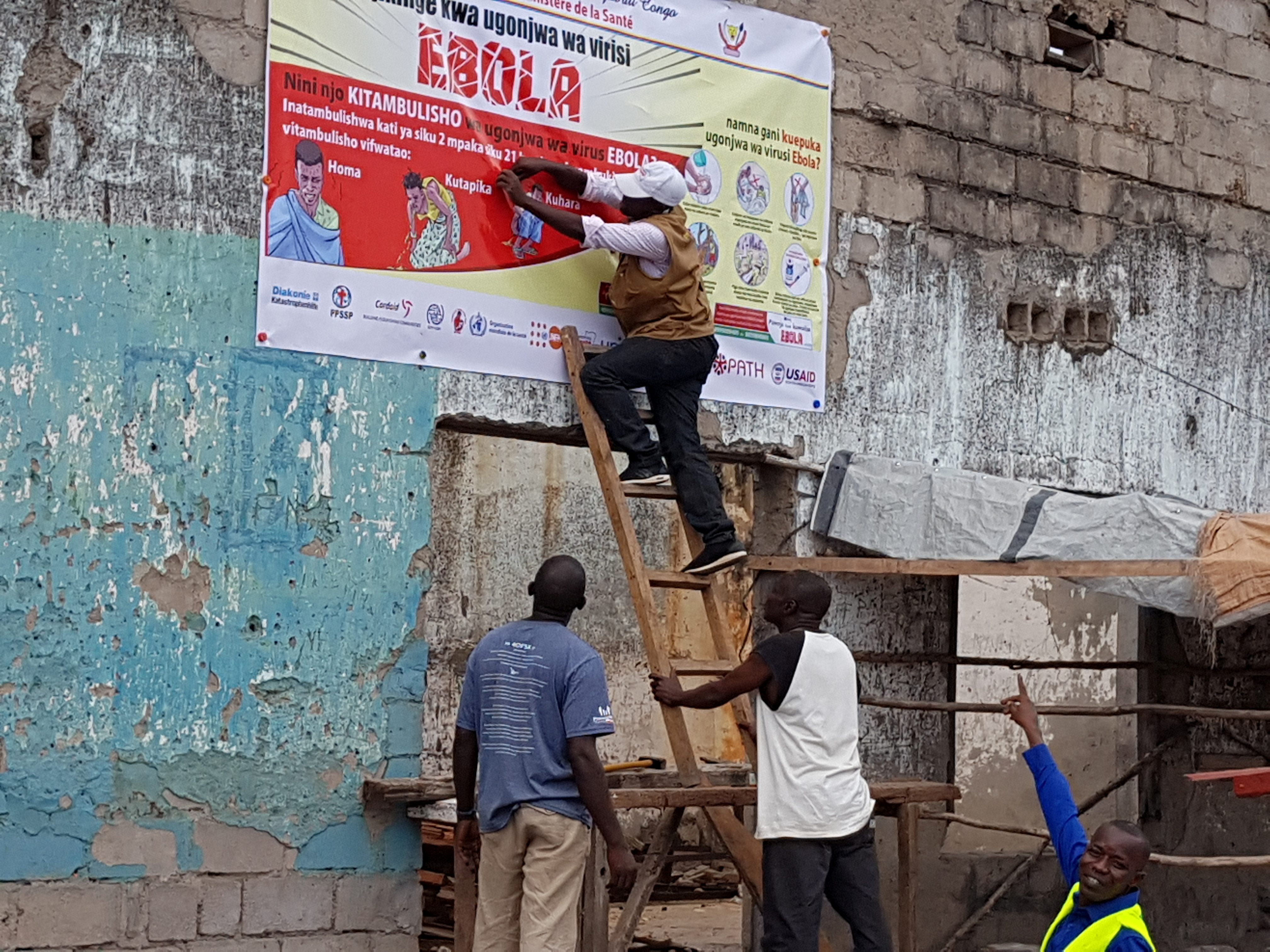 Workers fix an Ebola awareness poster in Tchomia, Congo, to raise awareness about Ebola in the local community