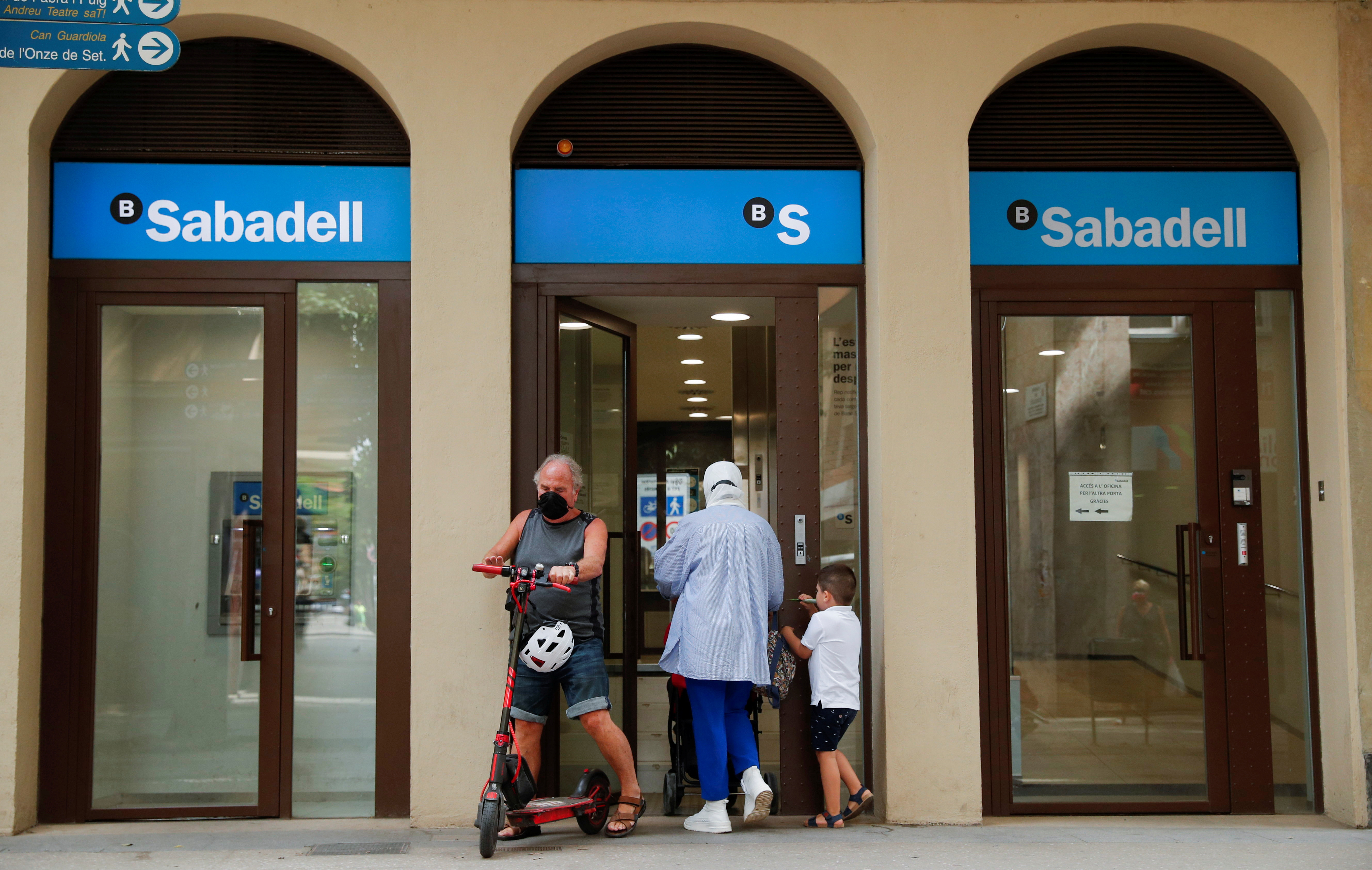 People walk at the door of a Sabadell bank office in Barcelona