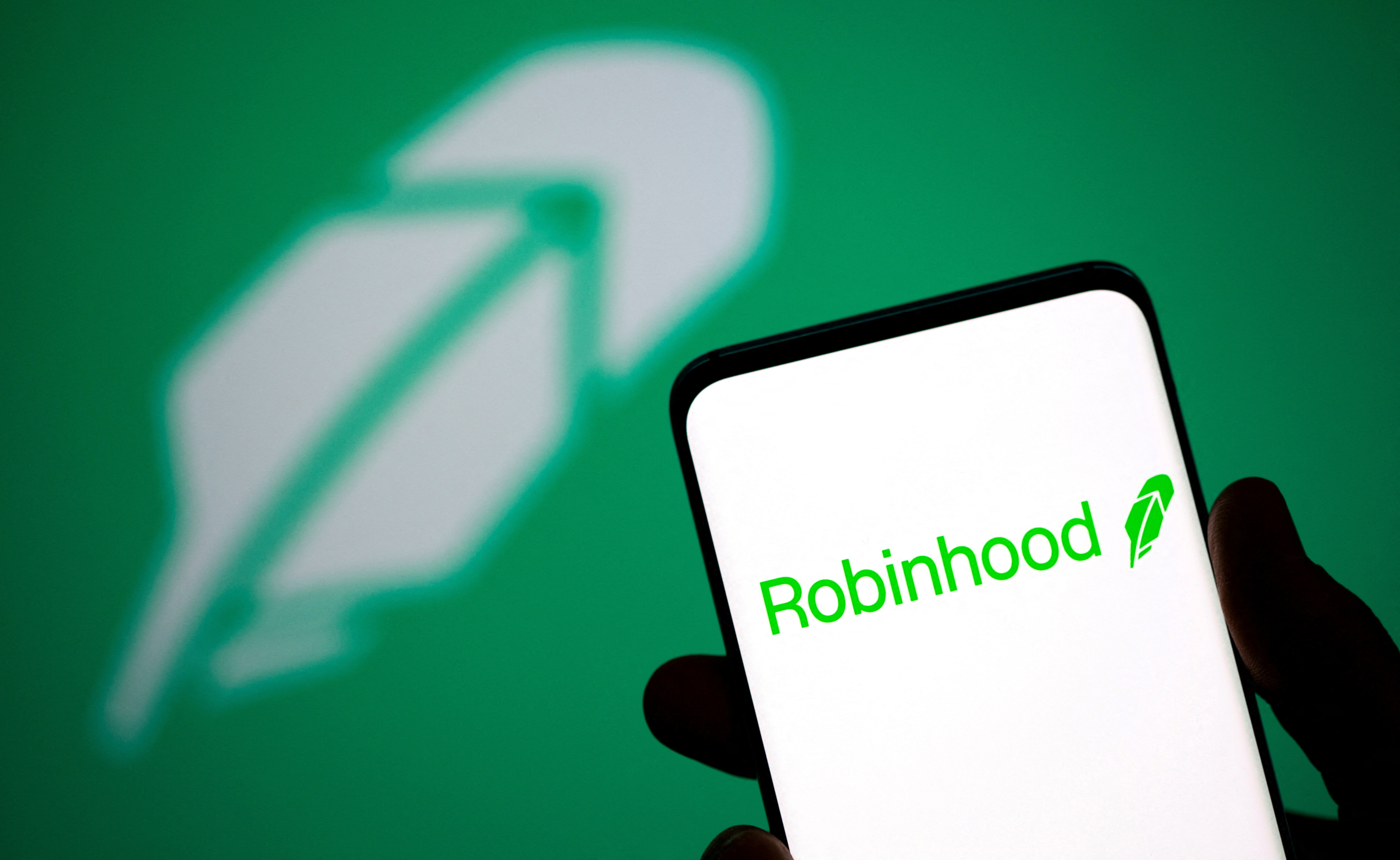 Robinhood logo is seen on a smartphone in front of a displayed same logo in this illustration taken