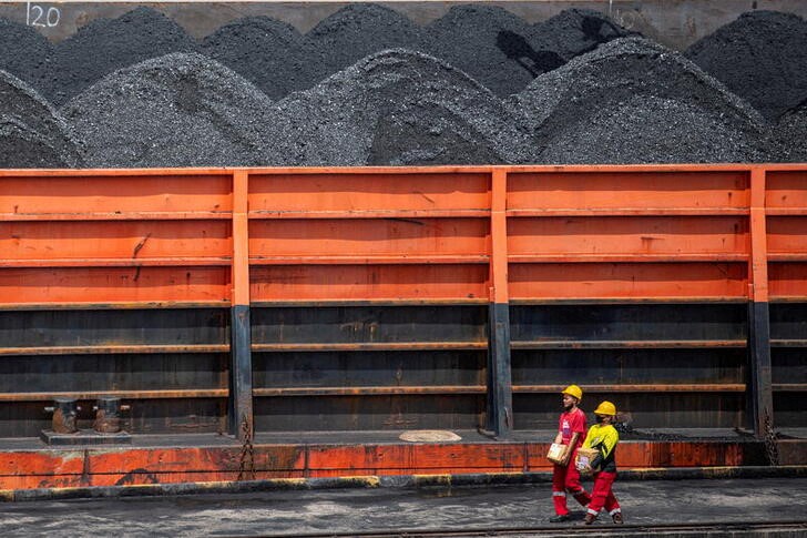 Workers walk near a tugboat carrying coal barges at a port in Palembang