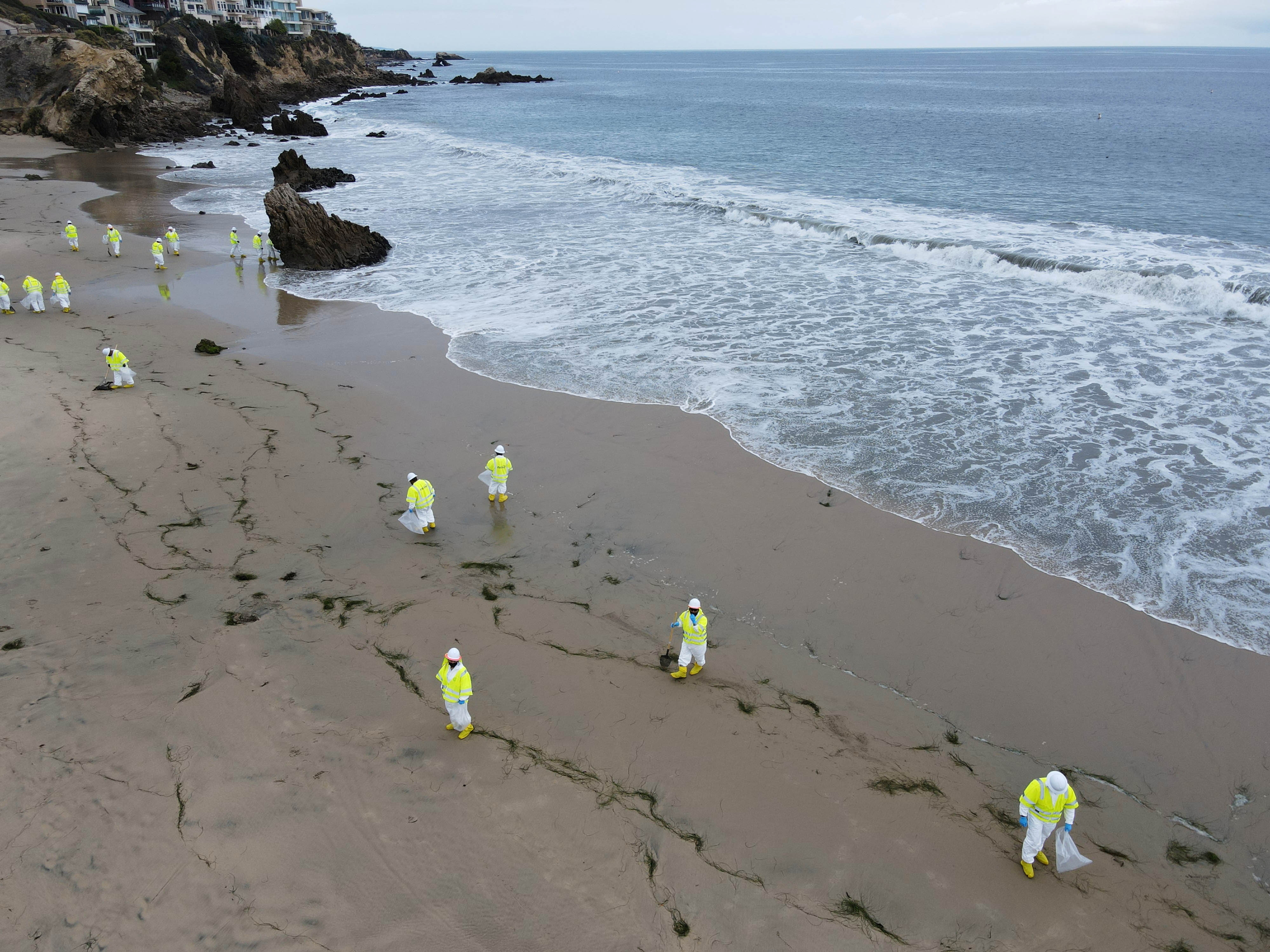 Workers rake up globs of crude oil after more than 3,000 barrels (126,000 gallons) of crude oil leaked from a ruptured pipeline into the Pacific Ocean in Corona Del Mar State Beach, Newport Beach, California, U.S. October 7, 2021. Picture taken with a drone. REUTERS/David Swanson