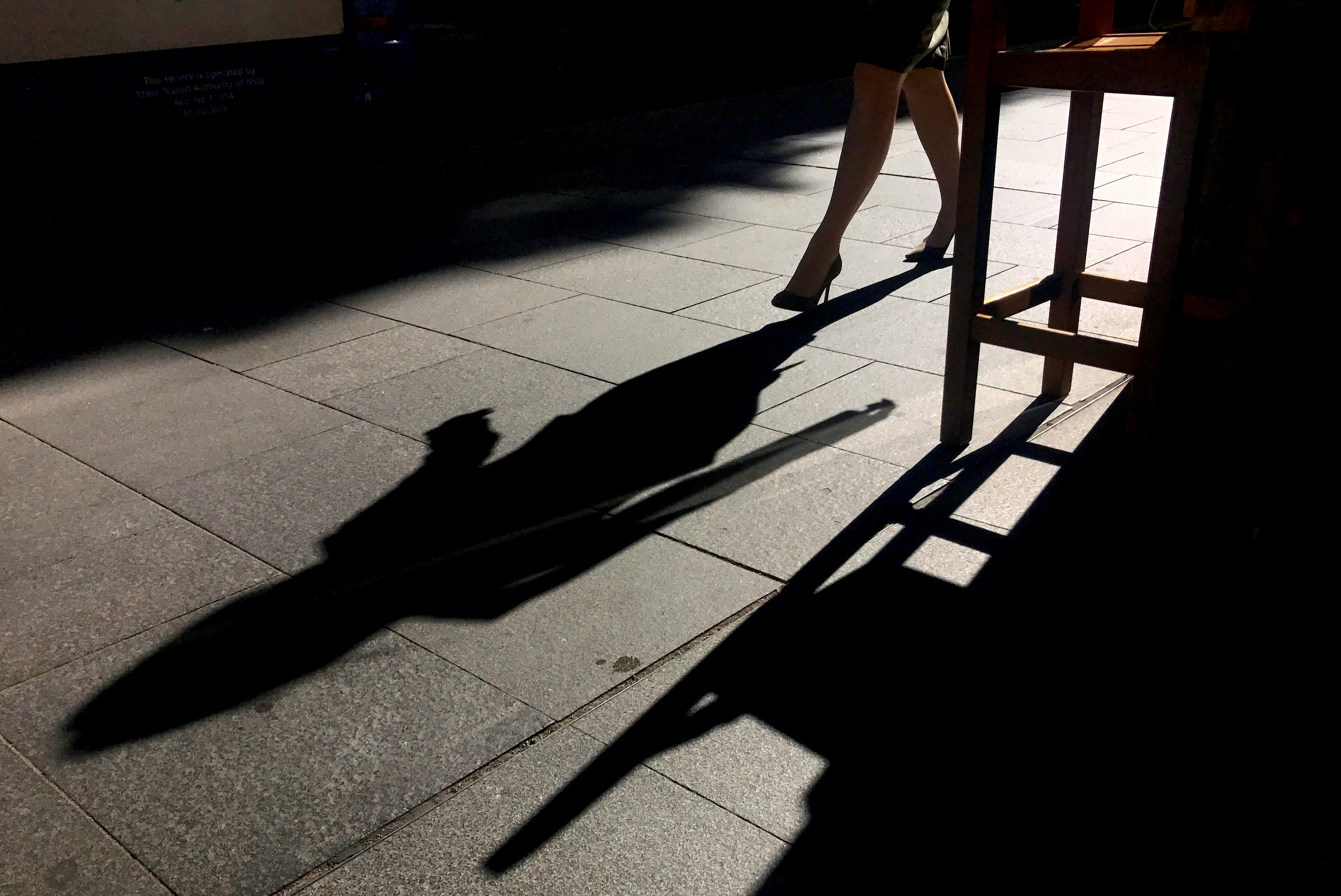 A woman casts a shadow as she walks along a footpath past a coffee shop on a sunny, winter day in central Sydney