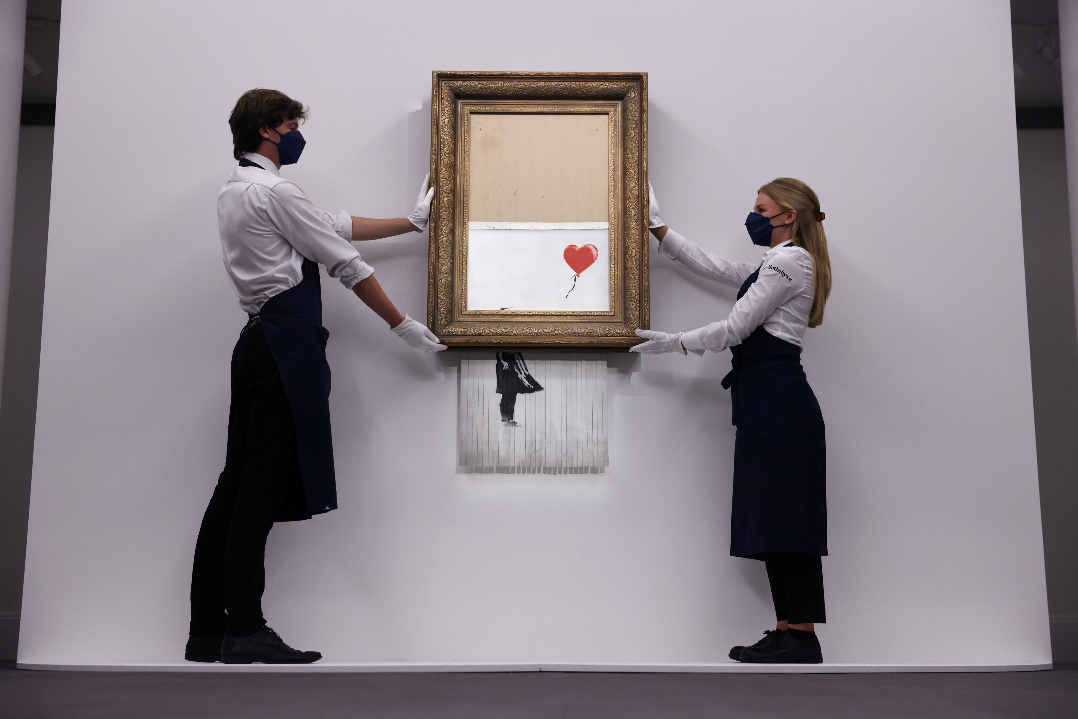 A gallery assistant poses by 'Love is in the Bin', an artwork by Banksy, which will be for sale in an auction, at Sotheby's in London, Britain, September 3, 2021. REUTERS/Tom Nicholson
