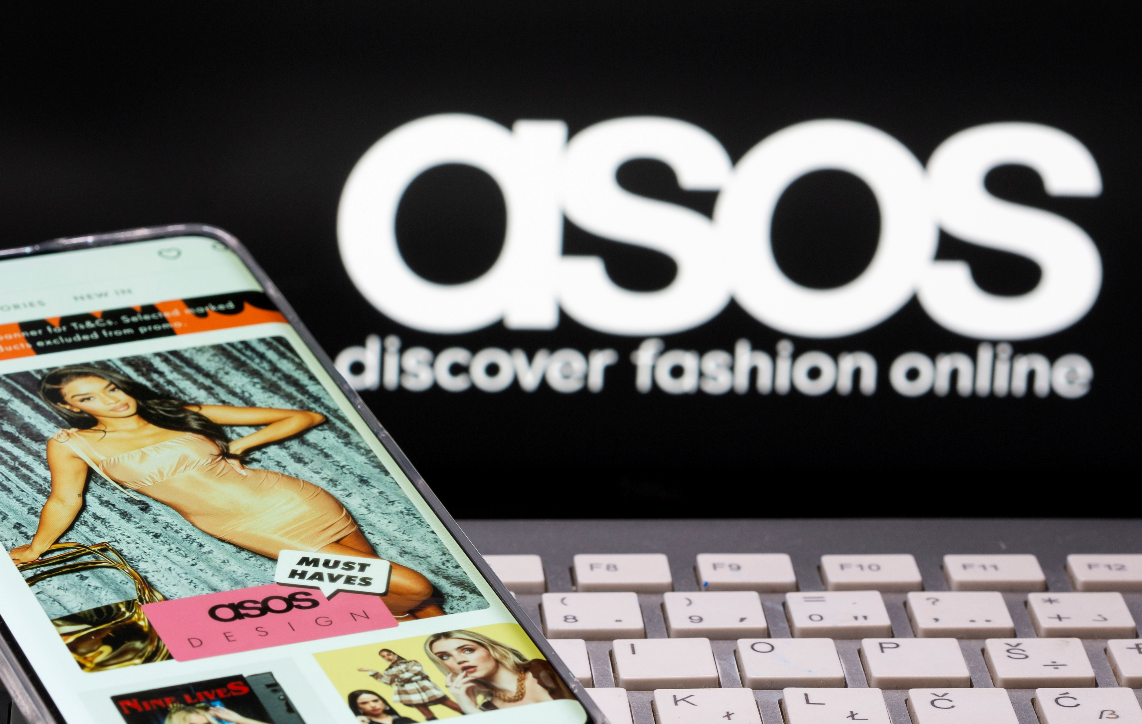 Smartphone with an ASOS app and a keyboard are seen in front of a displayed ASOS logo in this illustration picture