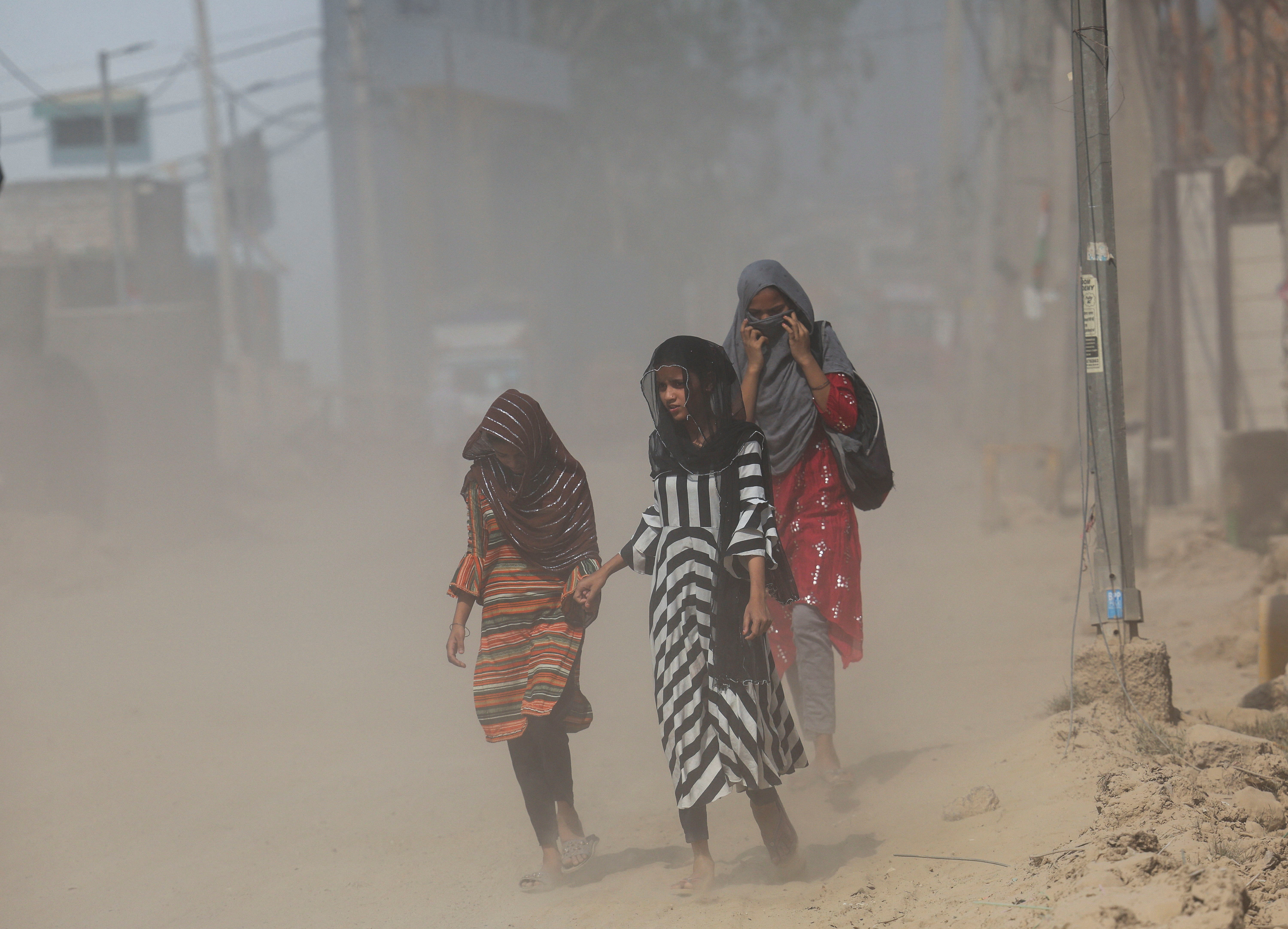 Girls cover their heads as they walk on a street near a landfill site on a hot summer day during a heatwave in New Delhi