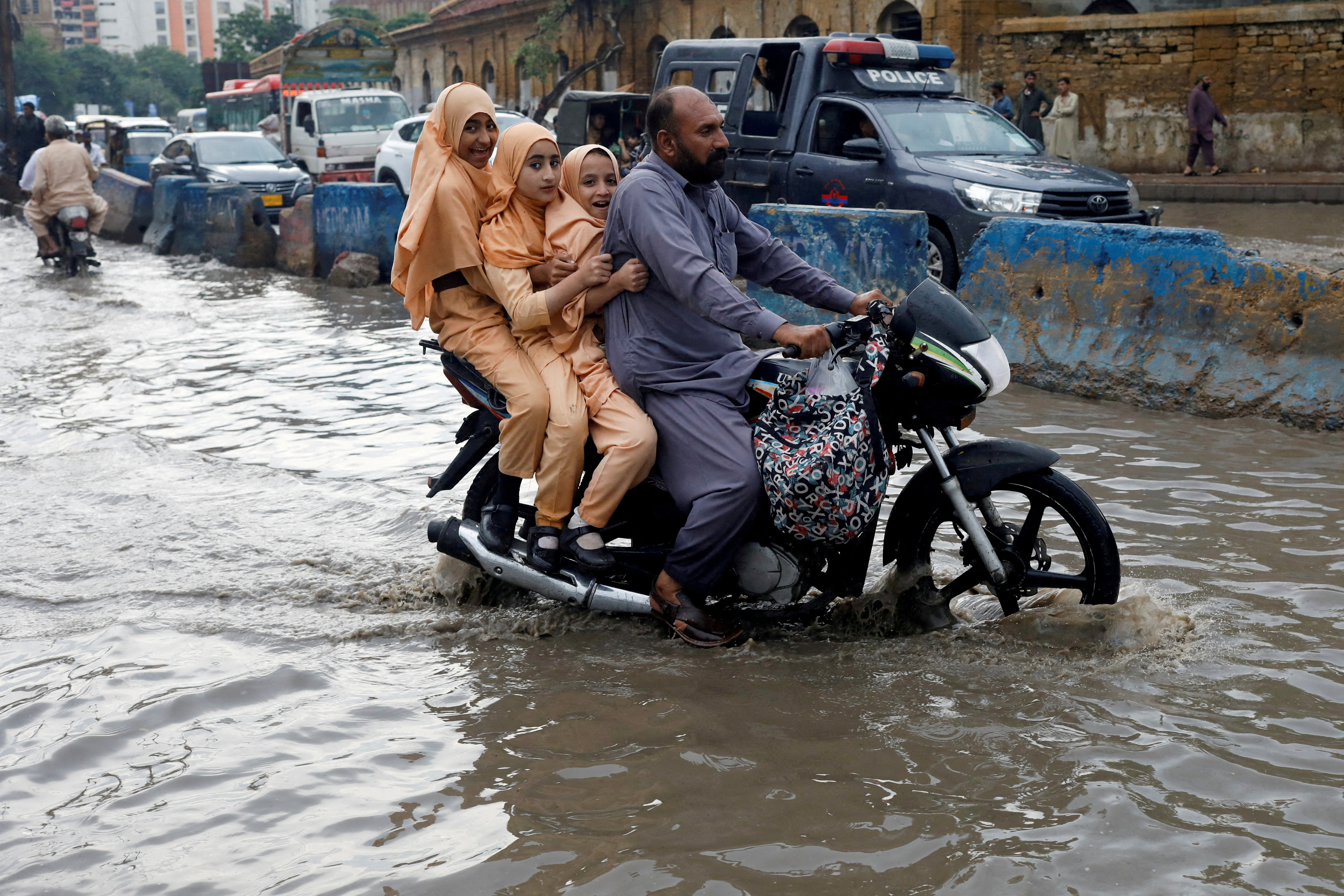 Man and students ride on a motorcycle on a flooded road, following rains during the monsoon season in Karachi