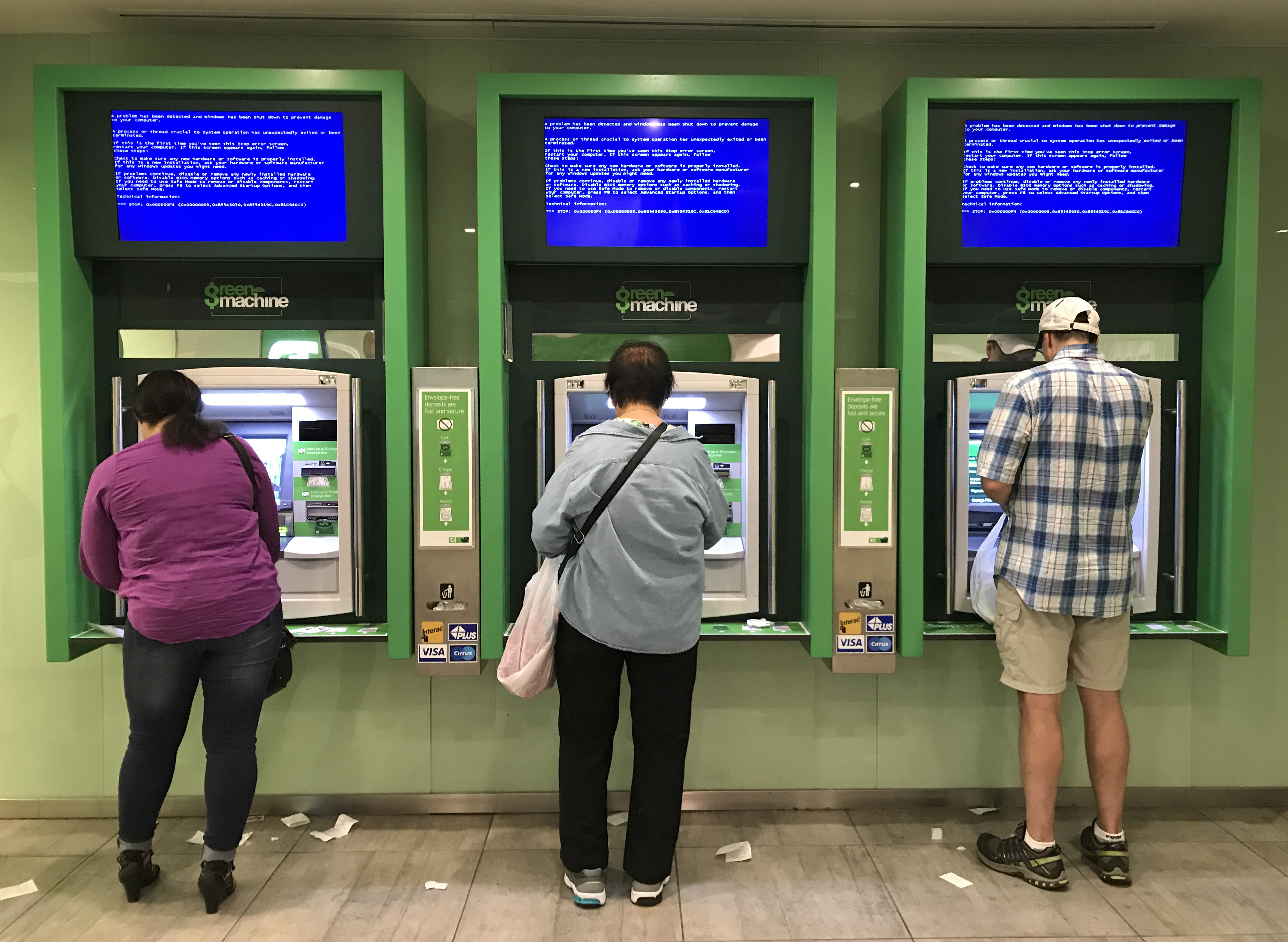 Customers use Toronto Dominion (TD) Bank ATM cash machines under video information screens showing a computer error in Toronto