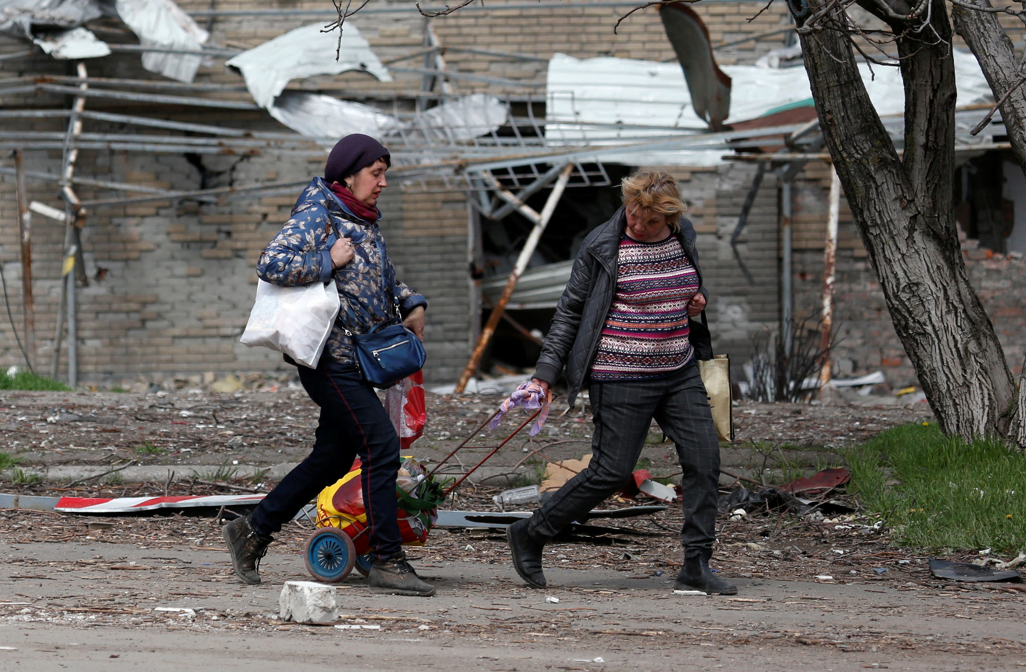 Women walk past a damaged building in Mariupol