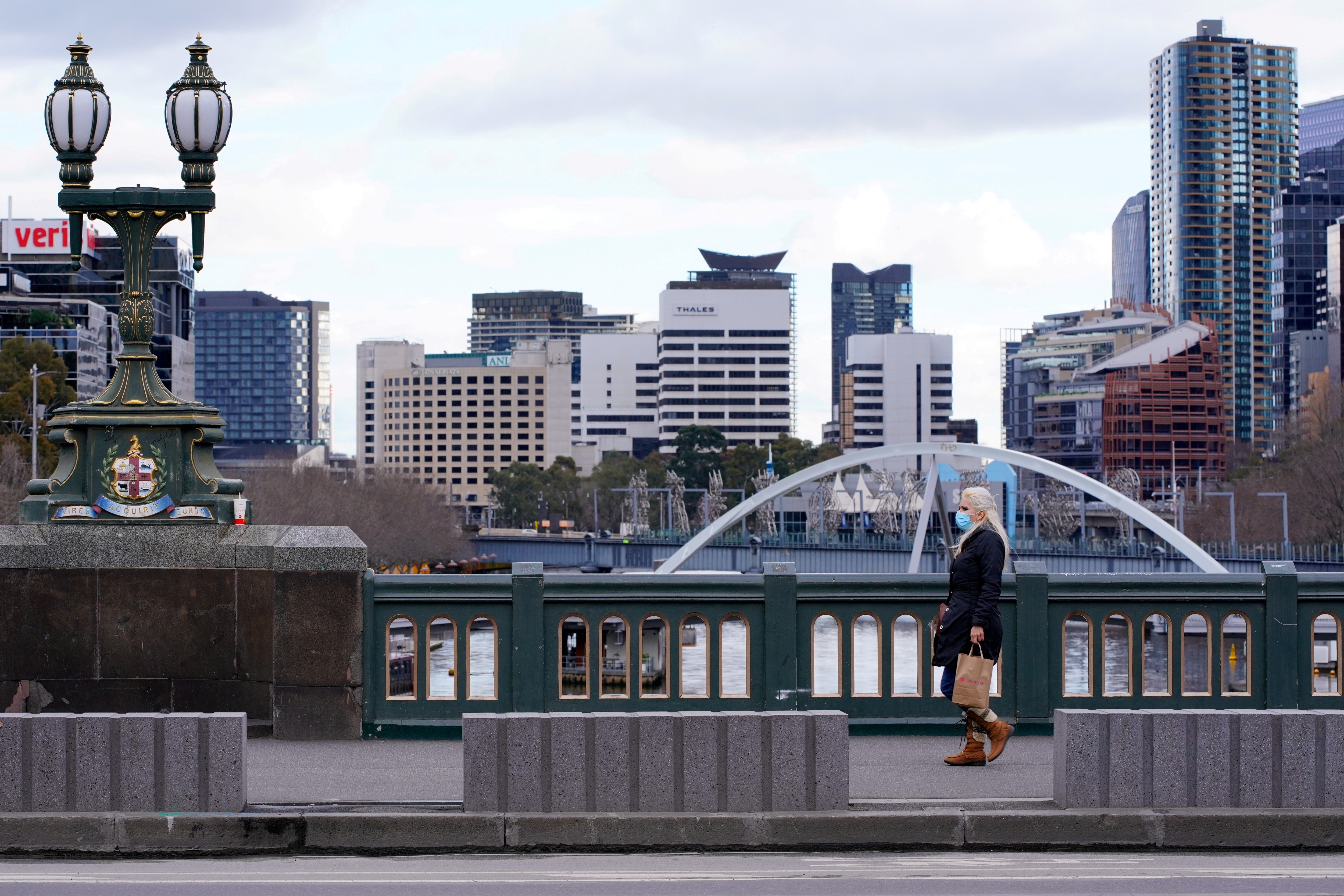 A lone woman, wearing a protective face mask, walks across a city centre bridge a in Melbourne