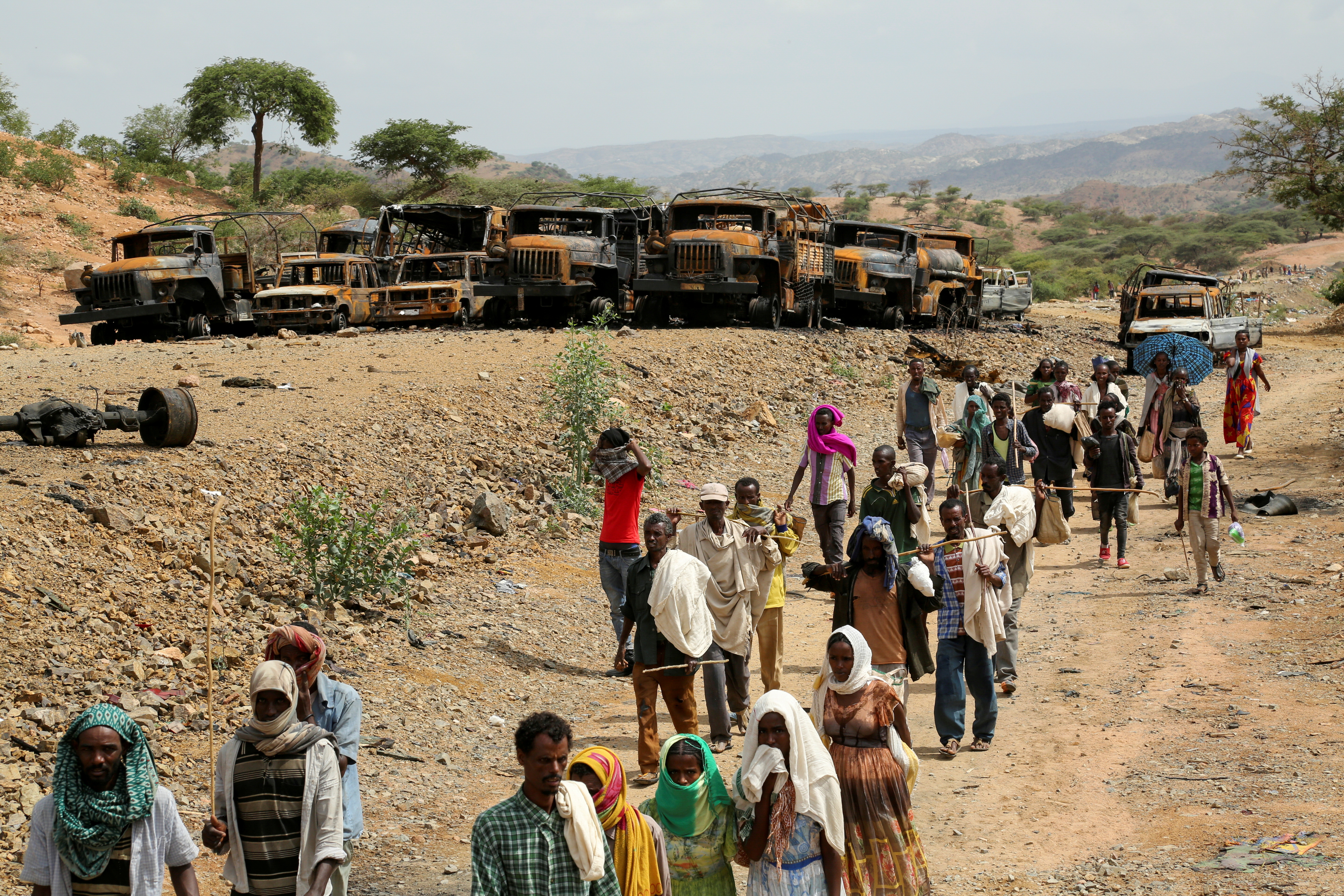 Villagers return from a market to Yechila town in south central Tigray walking past scores of burned vehicles, in Tigray