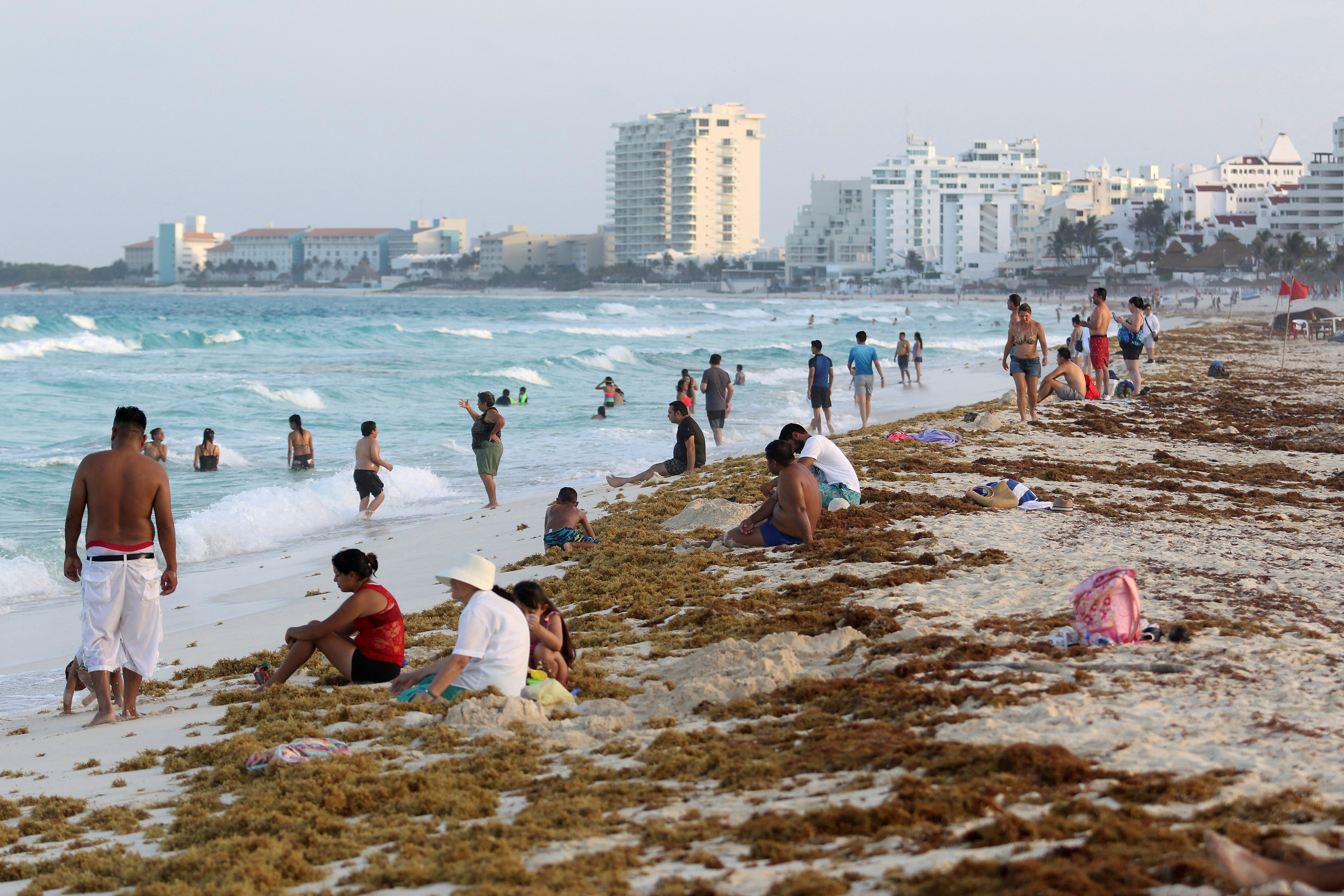 Tourists are seen on a beach covered with seaweed in Cancun