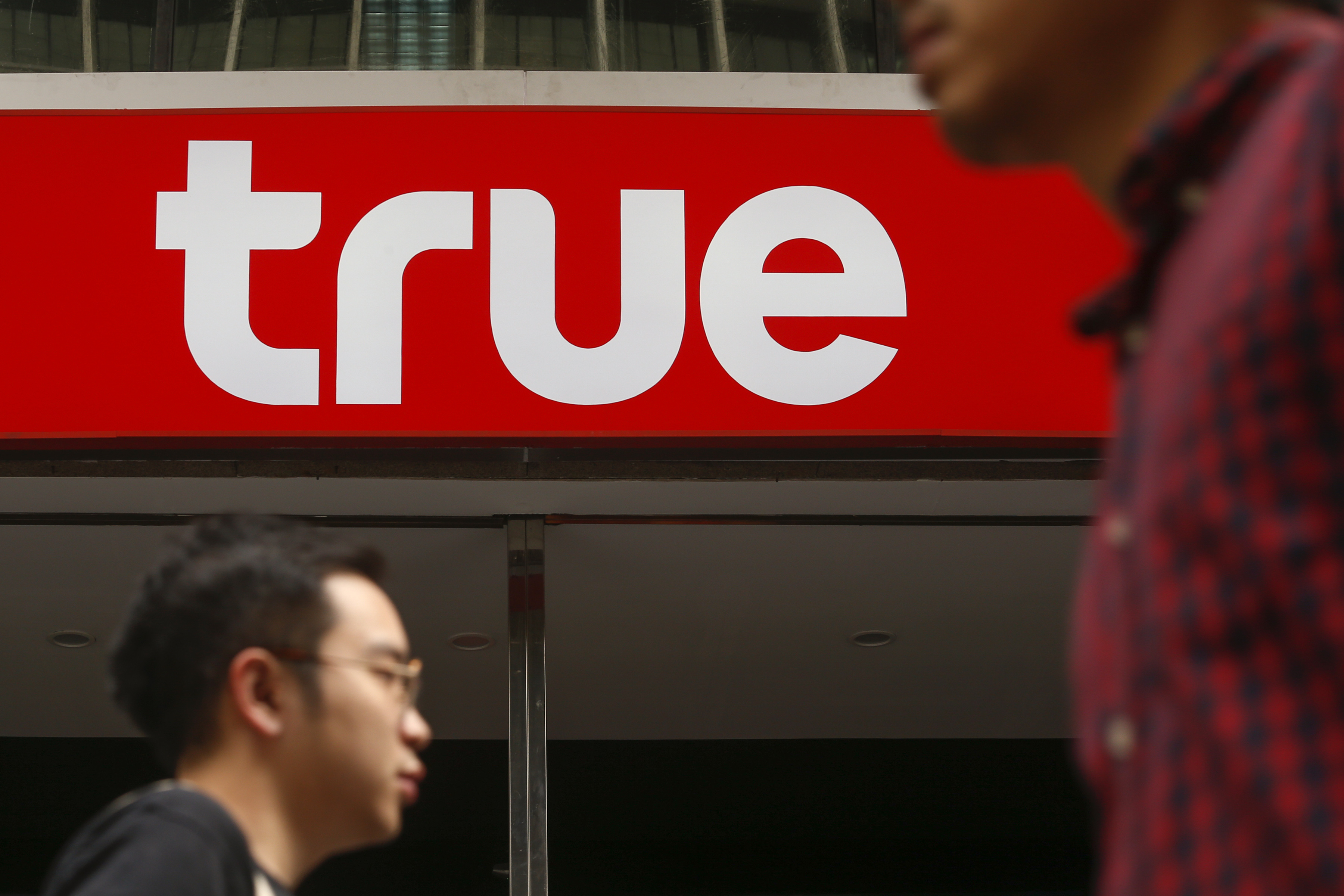 People walk past the logo of True Corp in Bangkok