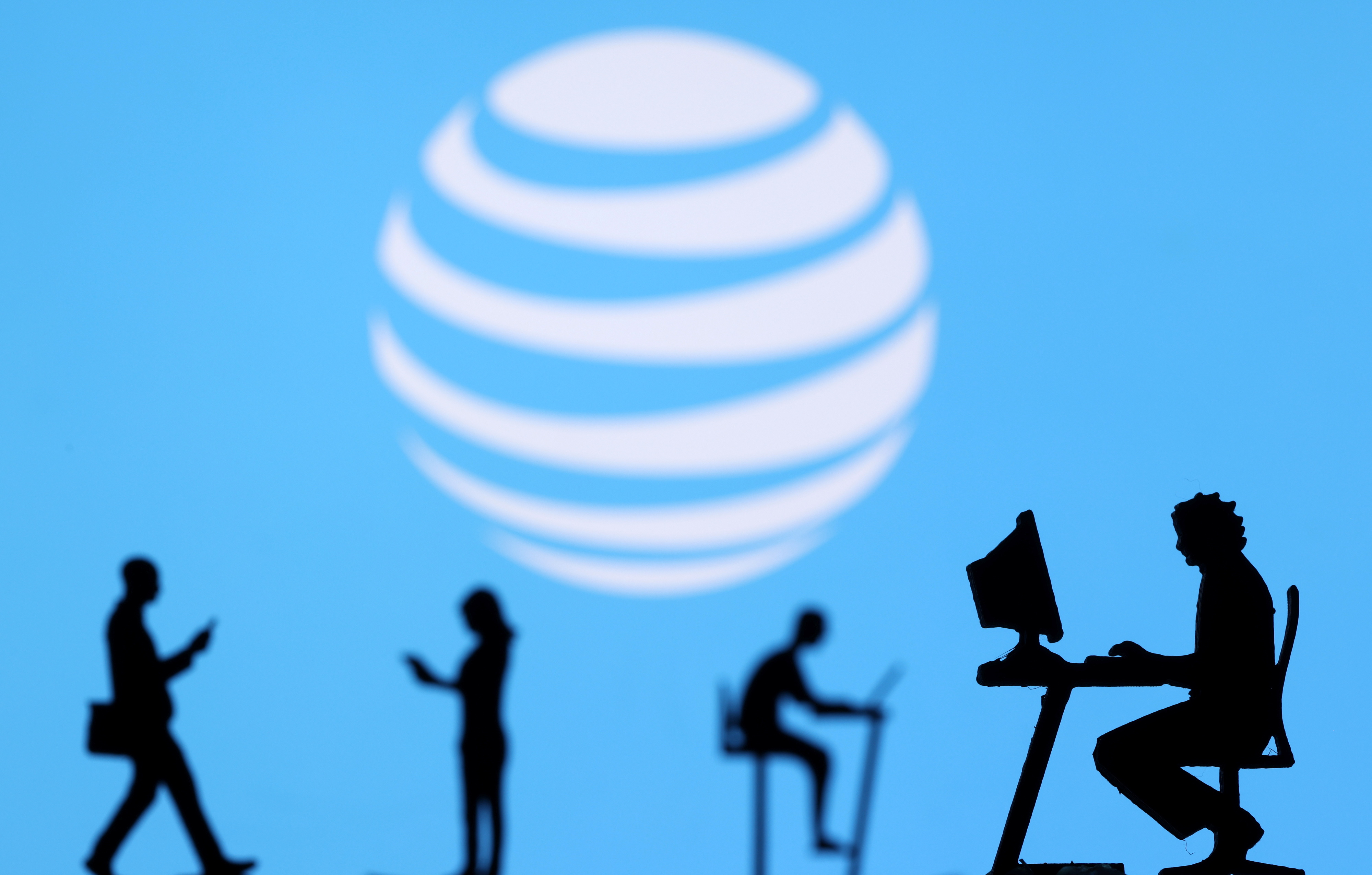 Illustration shows small toy figures with laptops and smartphones in front of displayed AT&T logo