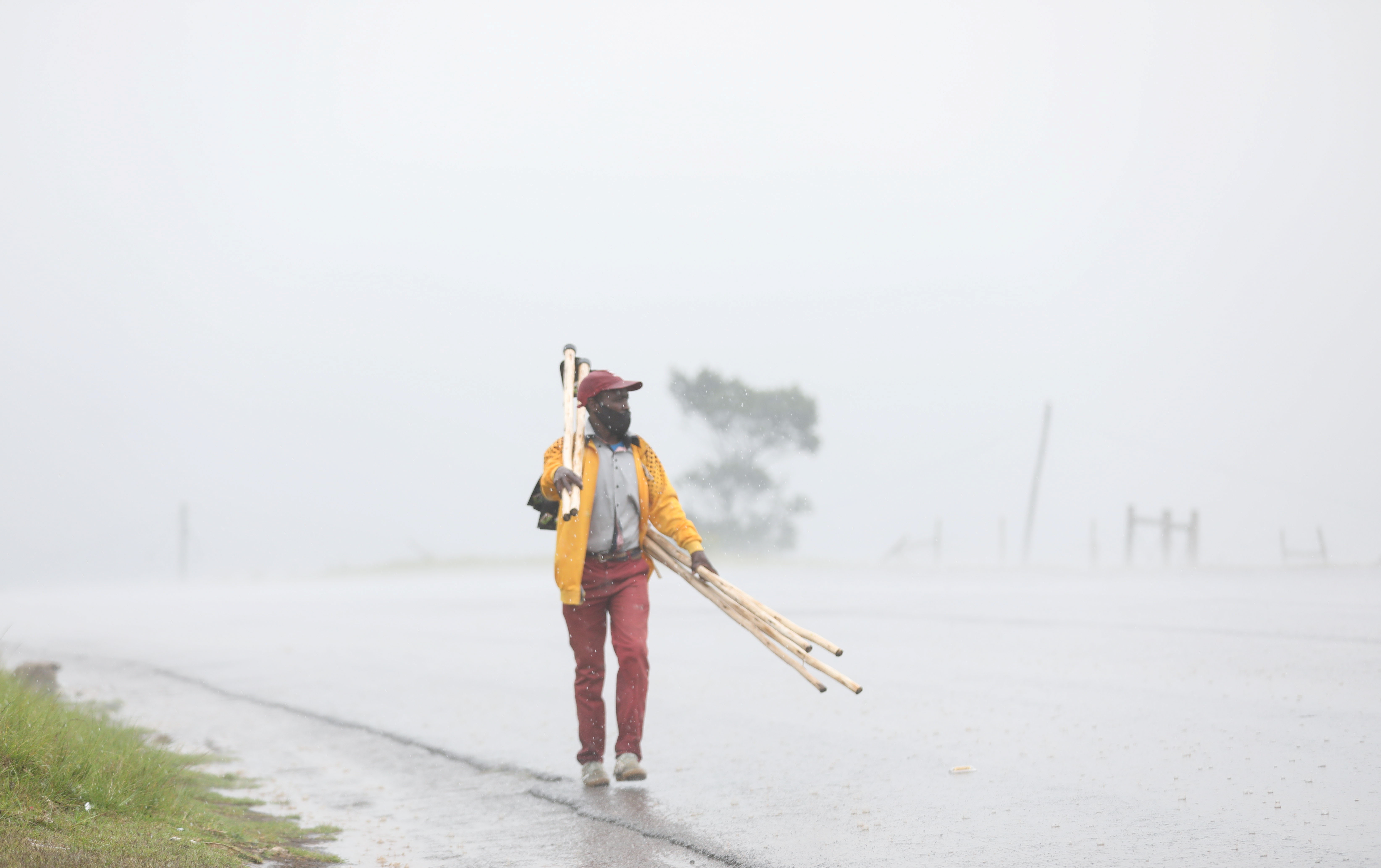 A man walks in the rain selling broom sticks, as the new Omicron coronavirus variant spreads, in Nqamakwe