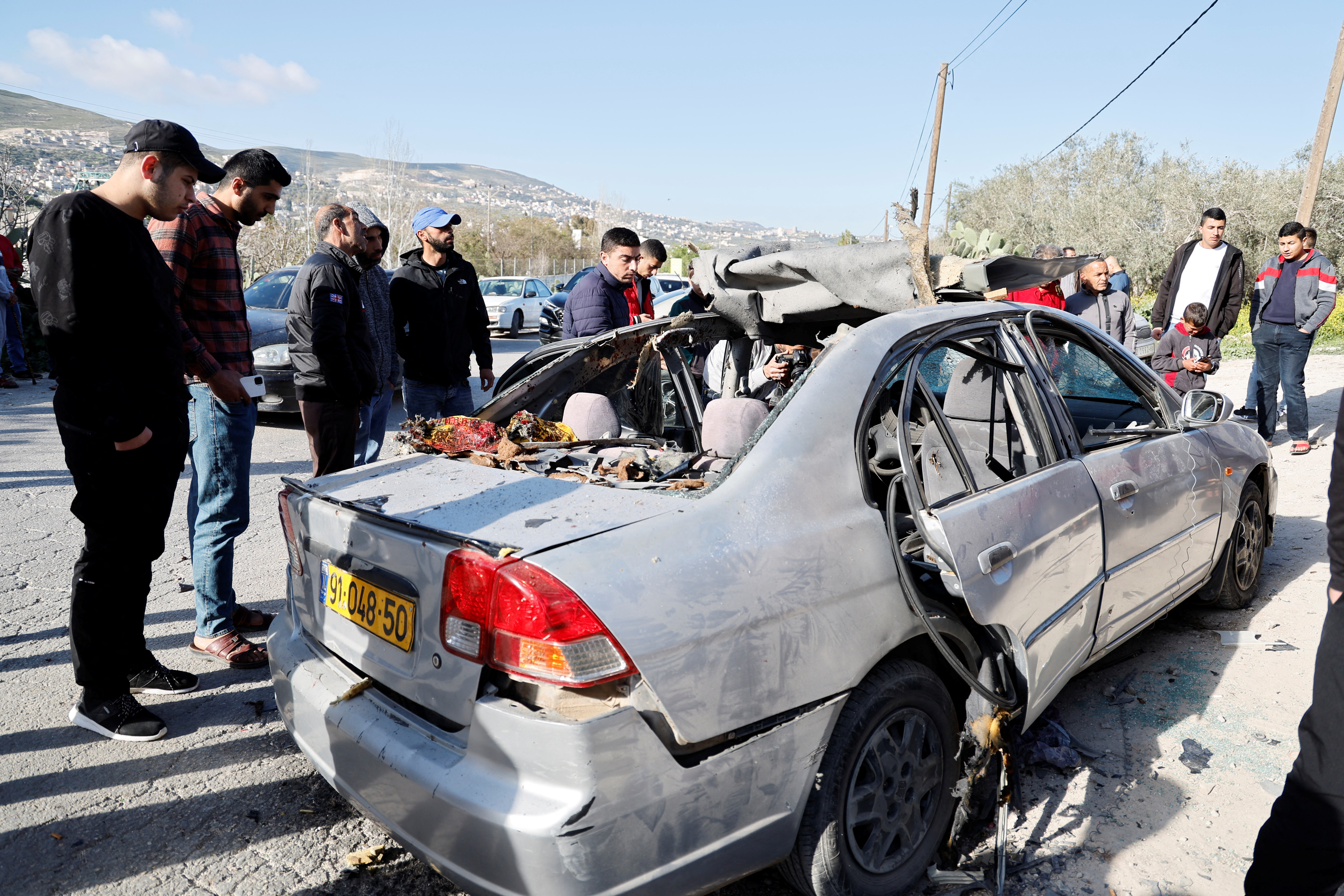 People look at a damaged car where three Palestinian militants were killed during an Israeli operation, near Jenin