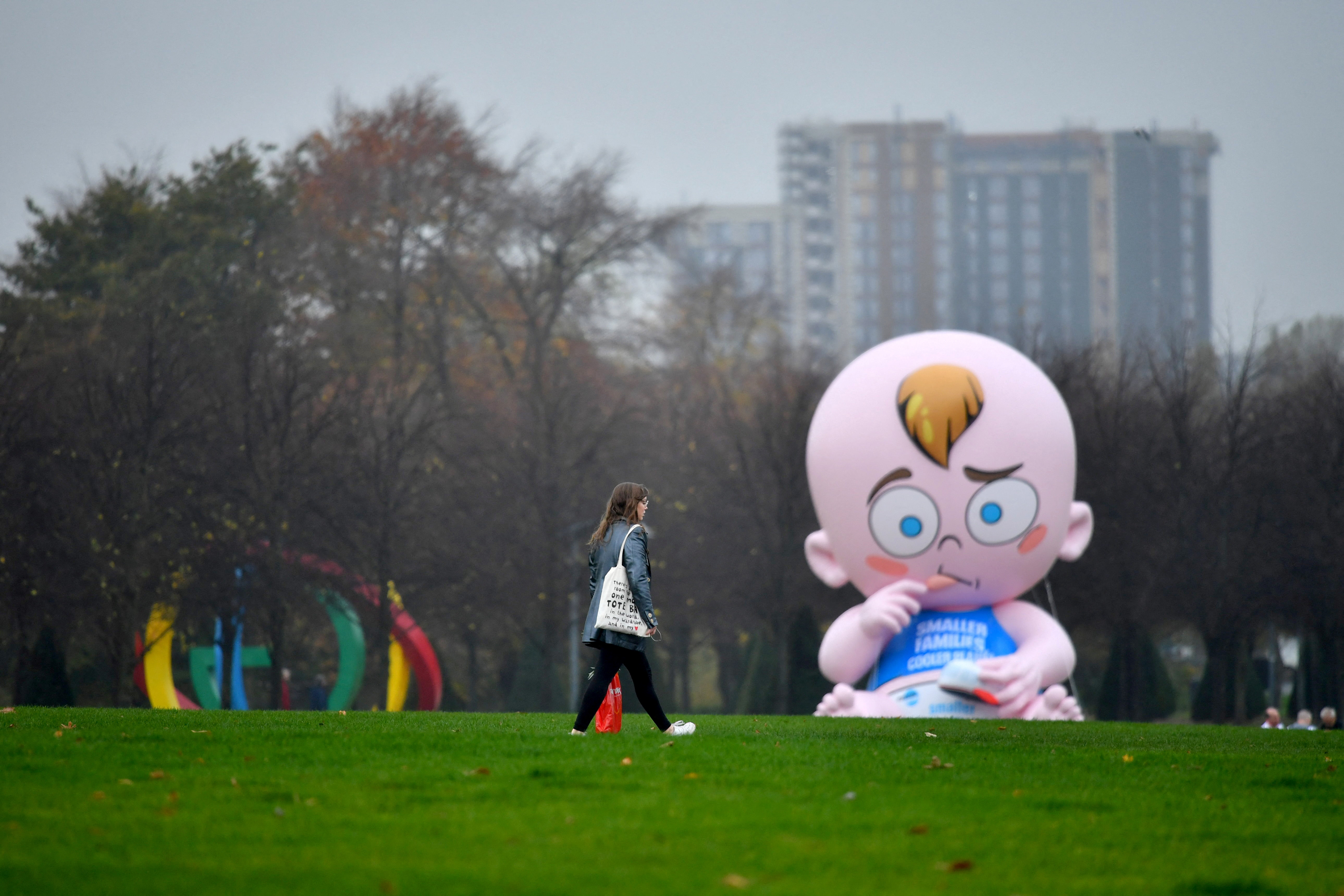 A woman walks past a giant baby balloon inflated by Climate Change activists in the rain at Glasgow Green as the UN Climate Change Conference (COP26) takes place, in Glasgow