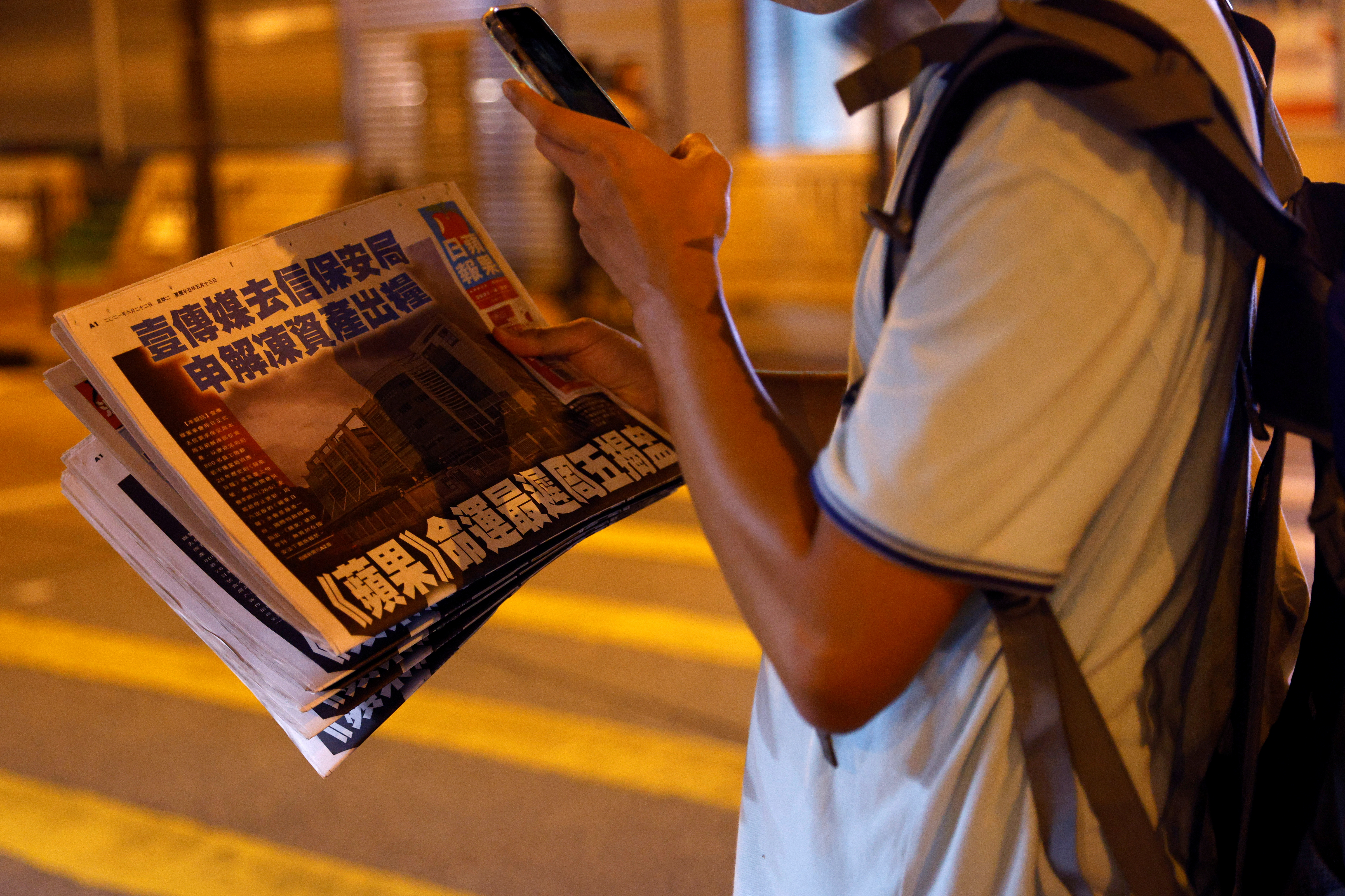 A man takes a photo of his copy of the Apple Daily newspaper after it looked set to close for good by Saturday following police raids and the arrest of executives in Hong Kong, China June 22, 2021. REUTERS/Tyrone Siu