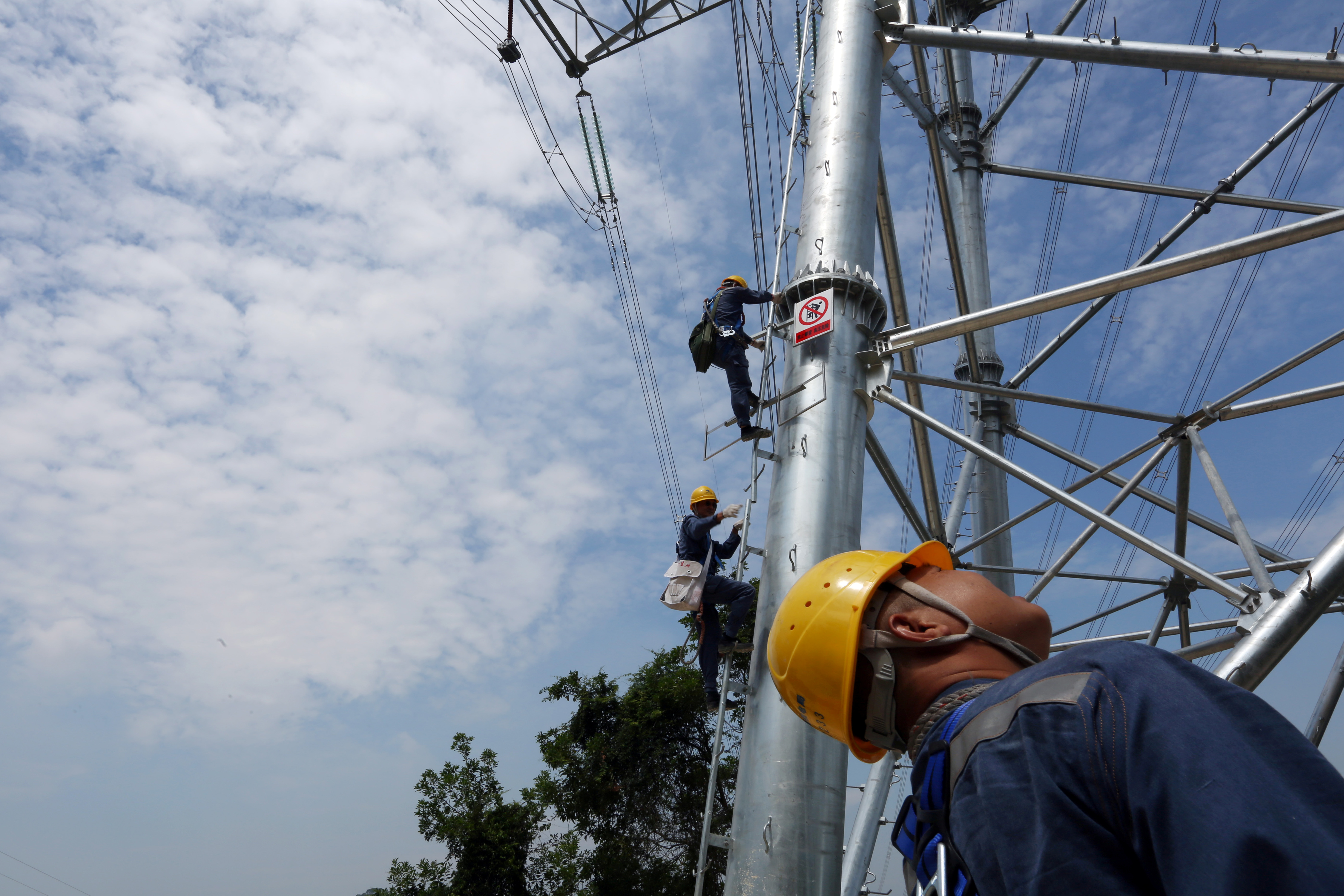Workers of grid operator China Southern Power Grid climb a transmission tower to inspect power cables in Dongguan