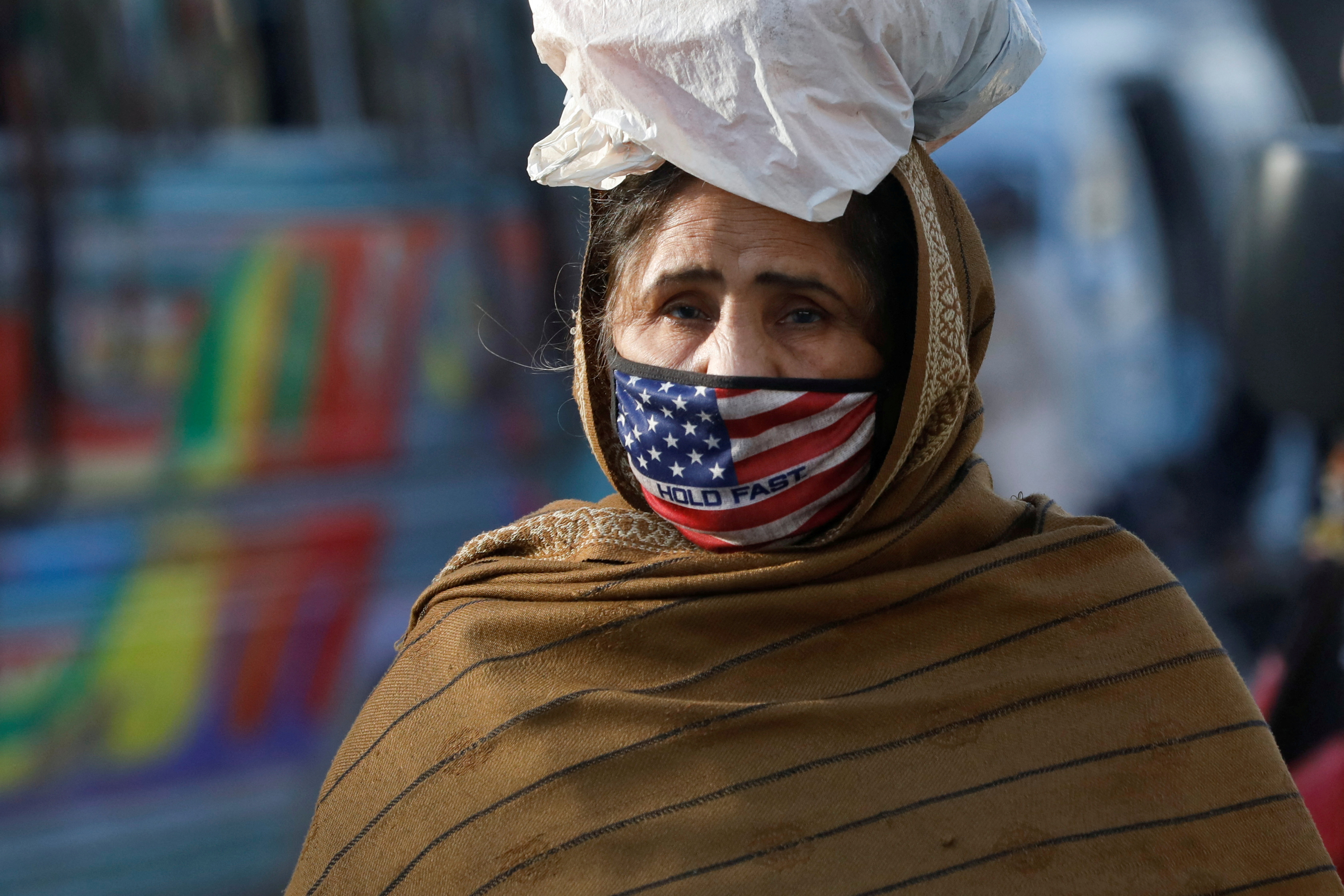 Woman wears a mask to prevent contracting COVID-19 as she carries a bag of supplies, in Karachi