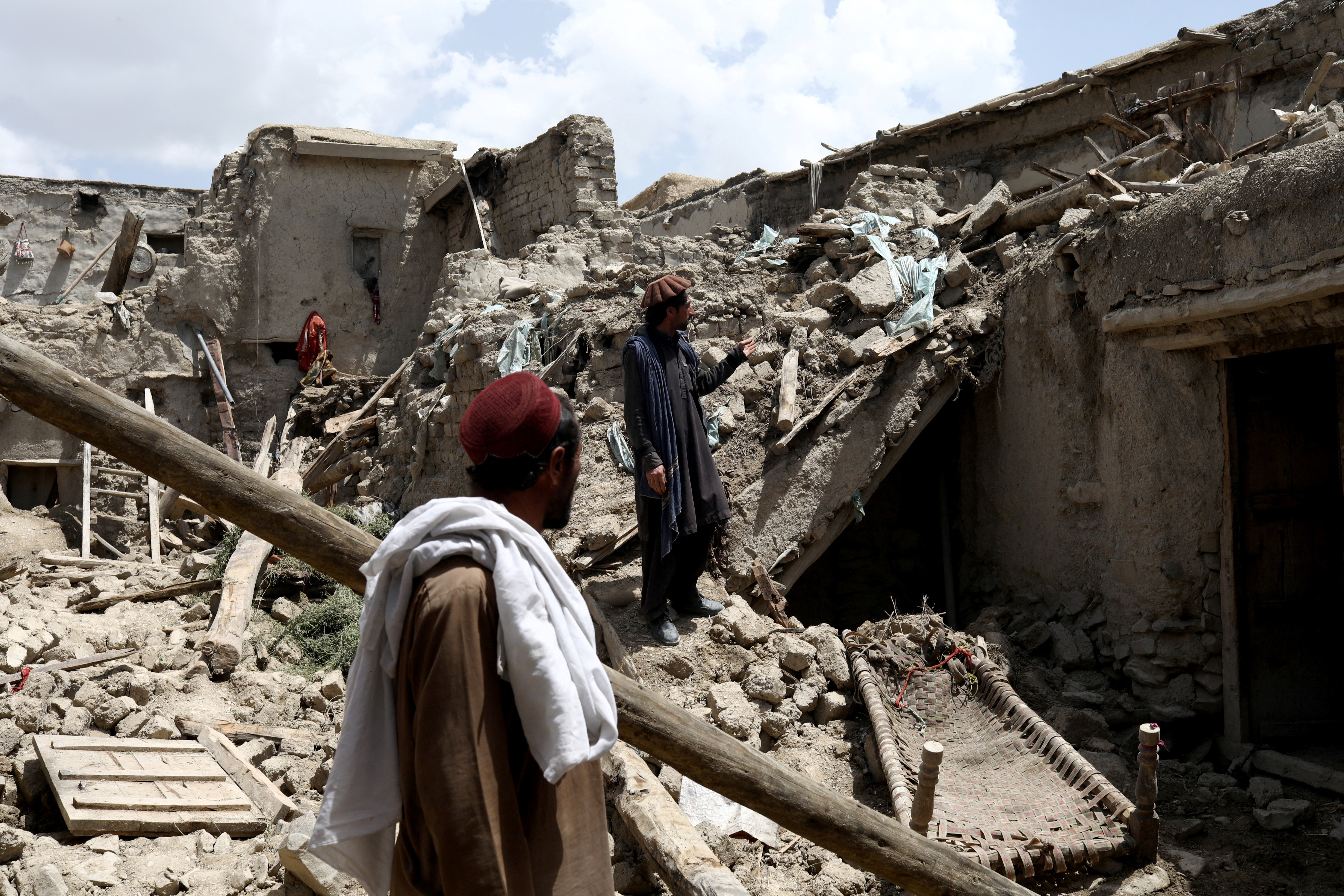 Afghan men stand on the debris of a house that was destroyed by an earthquake in Gayan