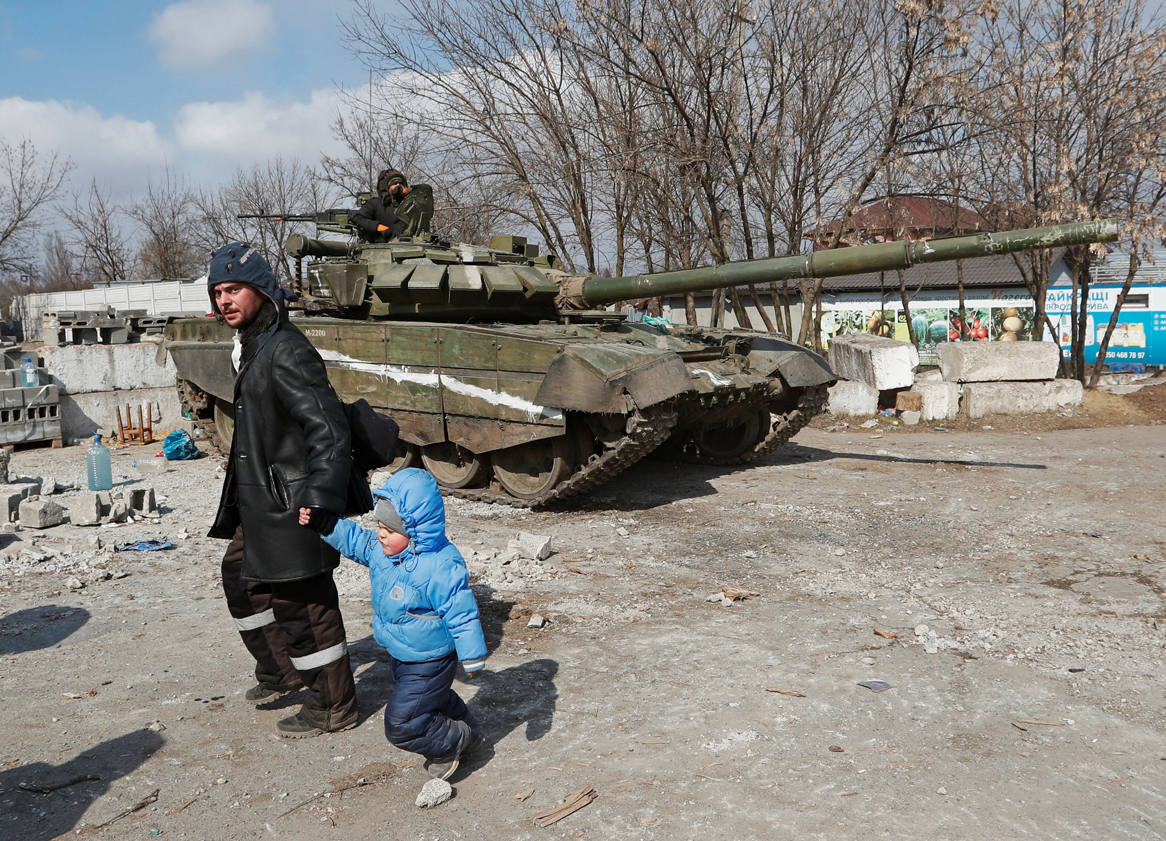 A local resident walks with a child past a tank of pro-Russian troops in the besieged city of Mariupol