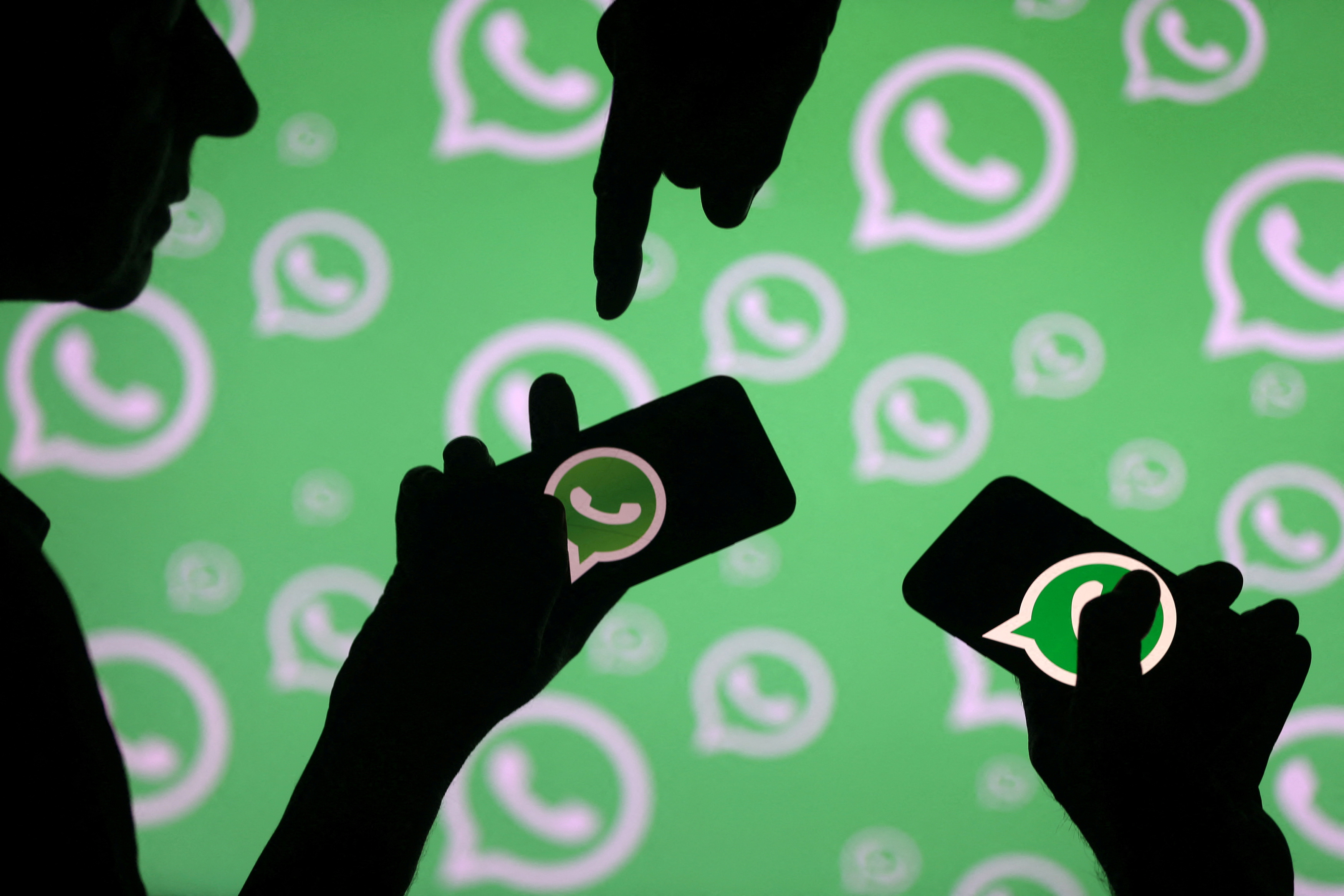 Men pose with smartphones in front of displayed Whatsapp logo