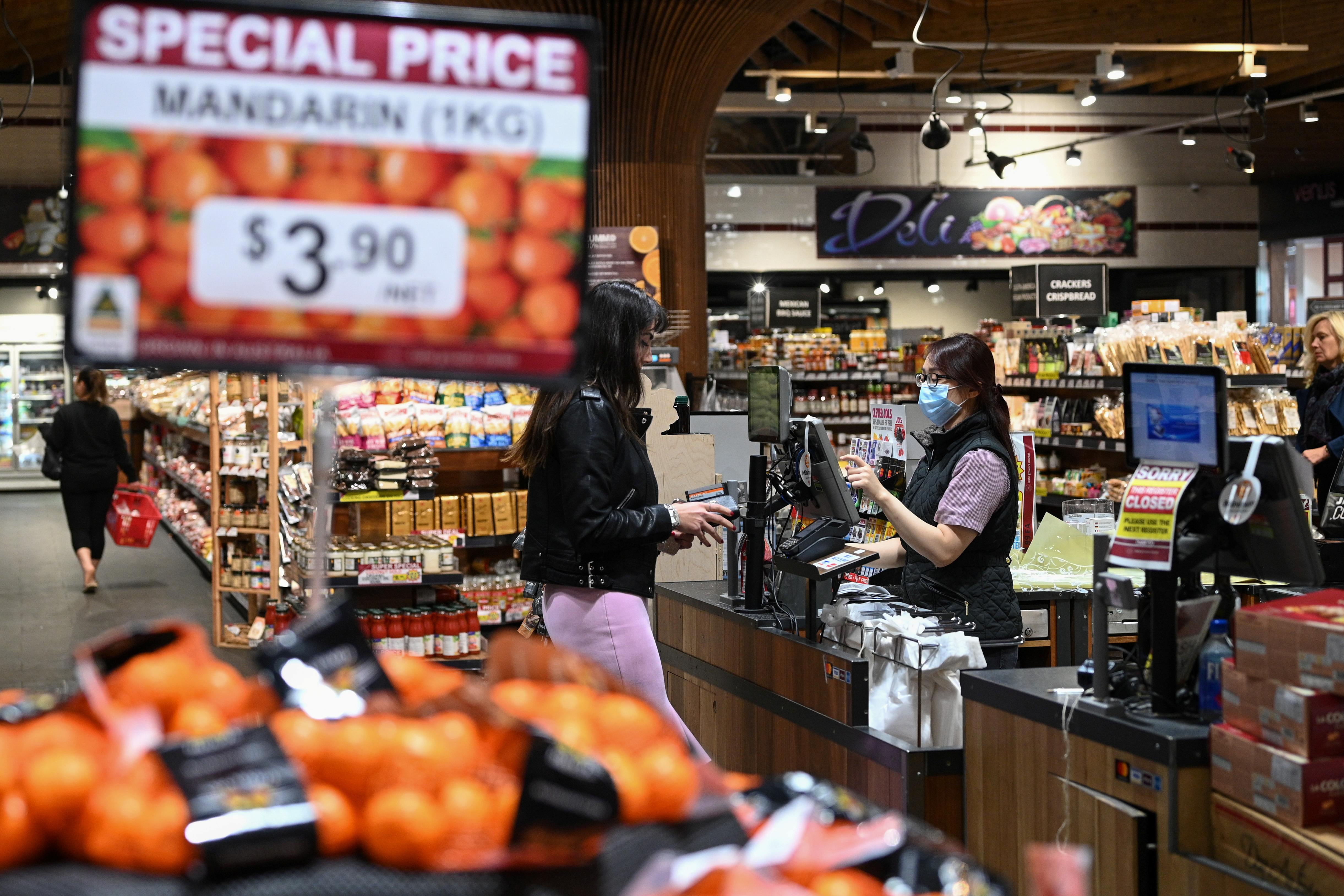 An employee wears a protective face mask while ringing up a customer at a specialty grocery store in Sydney