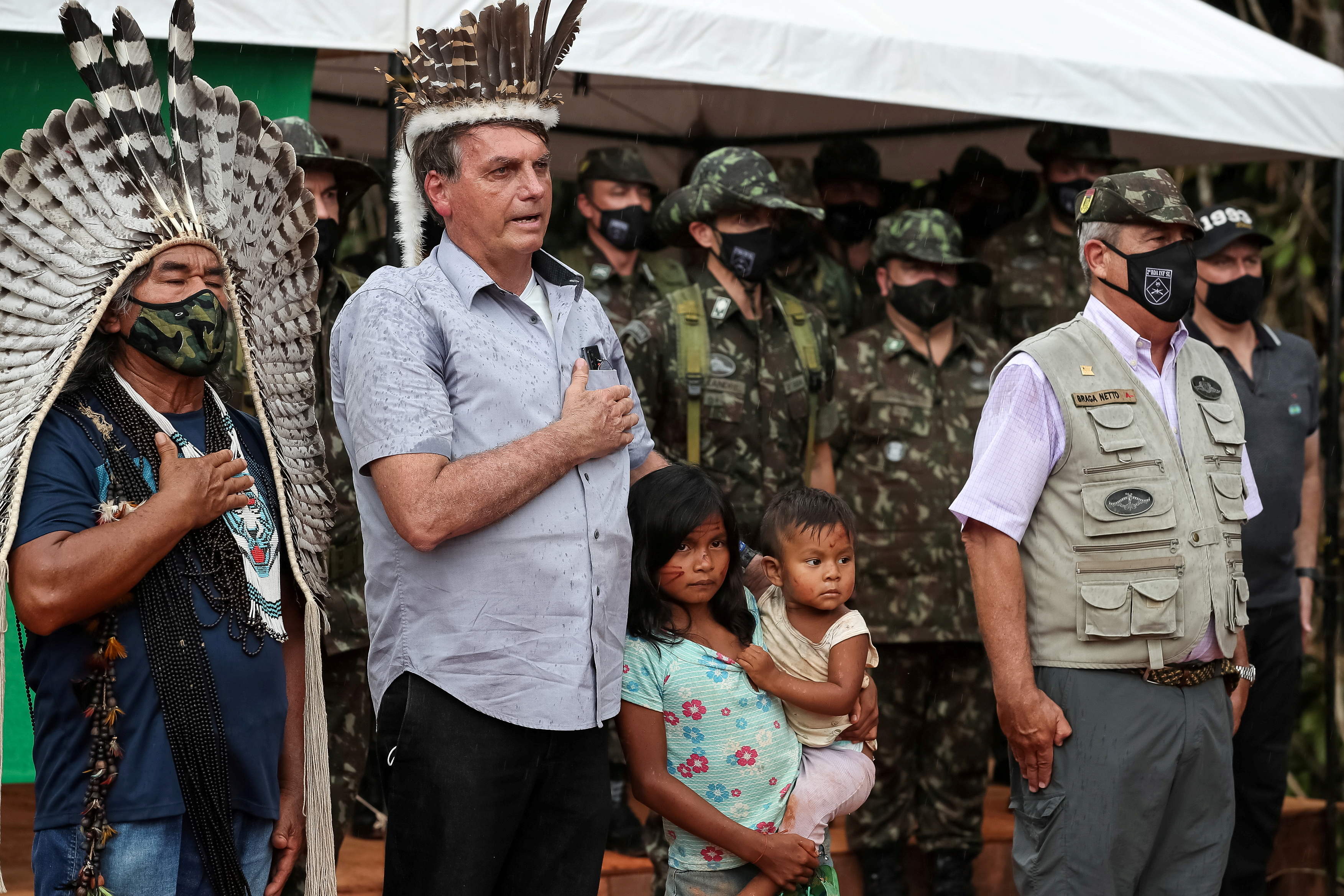 Brazil's President Jair Bolsonaro listens to national anthem next to a Tukano indigenous person in the Balaio reservation in the Upper Rio Negro river region of Amazonas state, bordering Colombia and Venezuela, near Sao Gabriel da Cachoeira, Brasil May 27, 2021.   Marcos Correa/Handout via REUTERS   