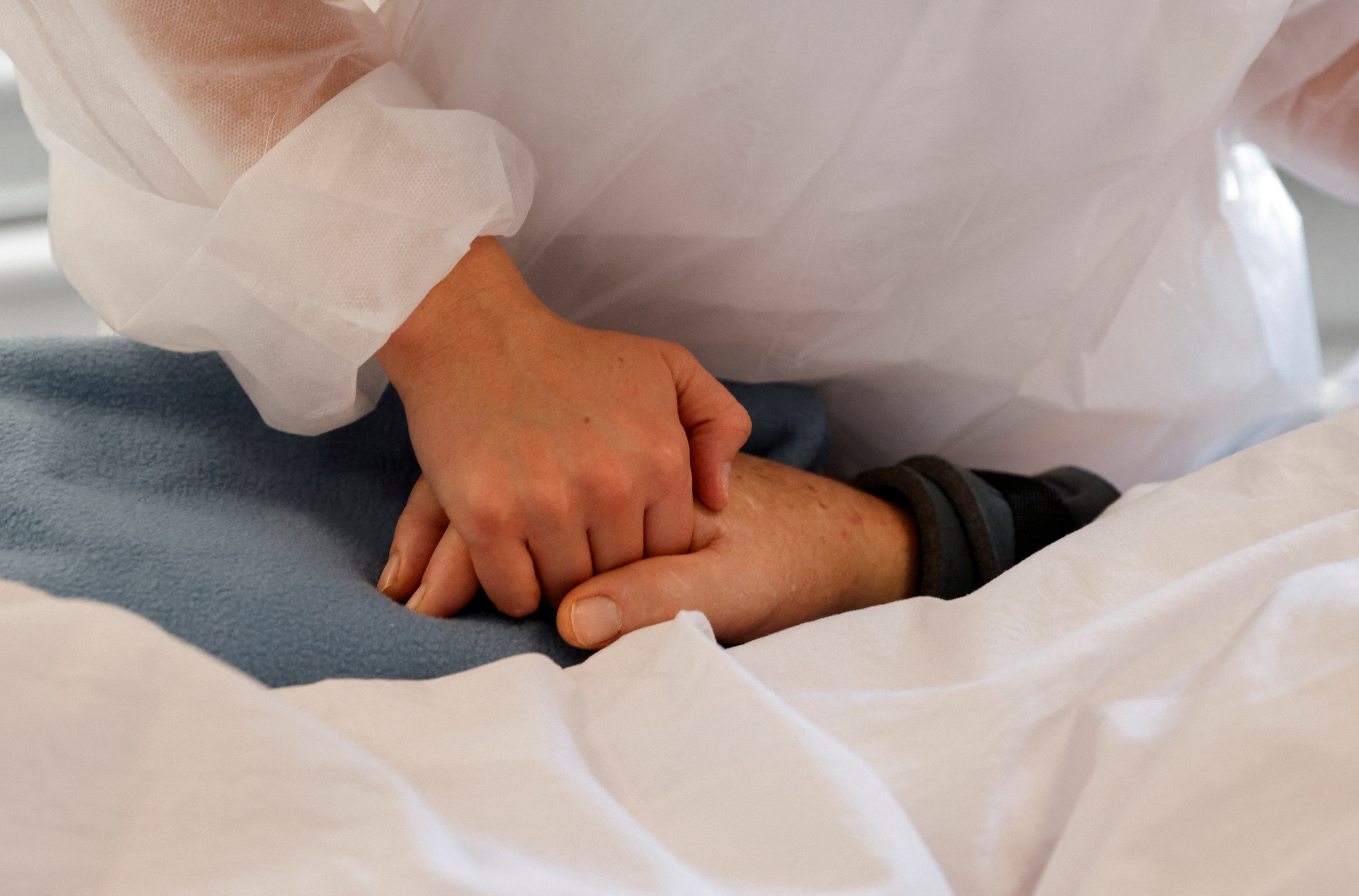 A nurse wearing a protective mask and suit holds the hand of a man in the Intensive Care Unit (ICU) where patients suffering from the coronavirus disease (COVID-19) are treated at Victor Provo hospital in Roubaix, France, November 6, 2020. REUTERS/Pascal Rossignol