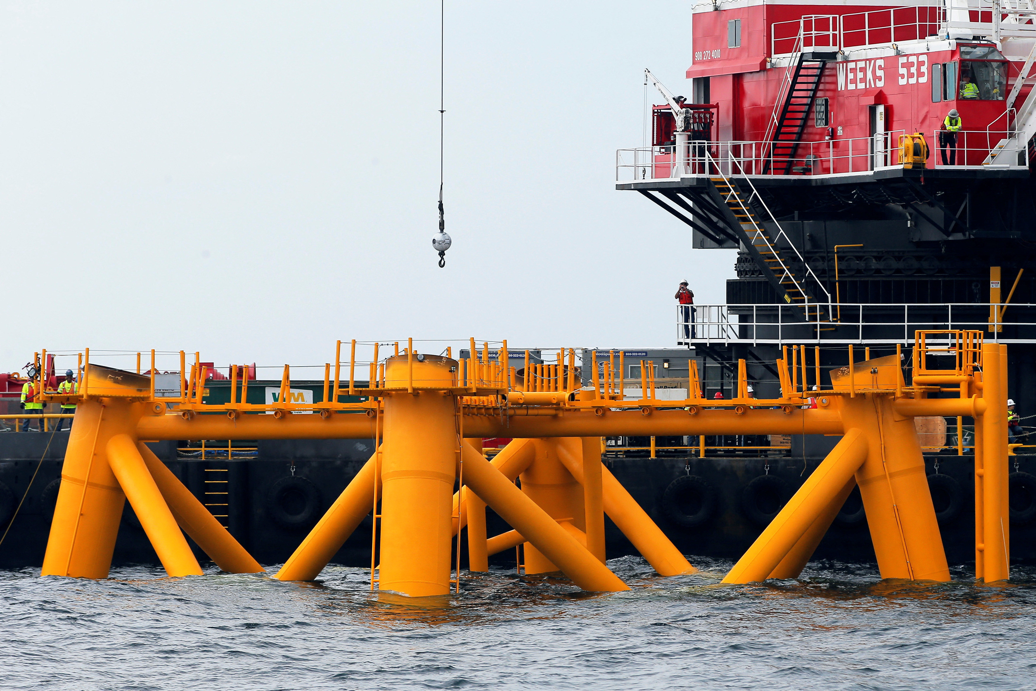 Workers look out from a construction barge next to the first jacket installed to support a turbine for a wind farm in the waters of the Atlantic Ocean off Block Island