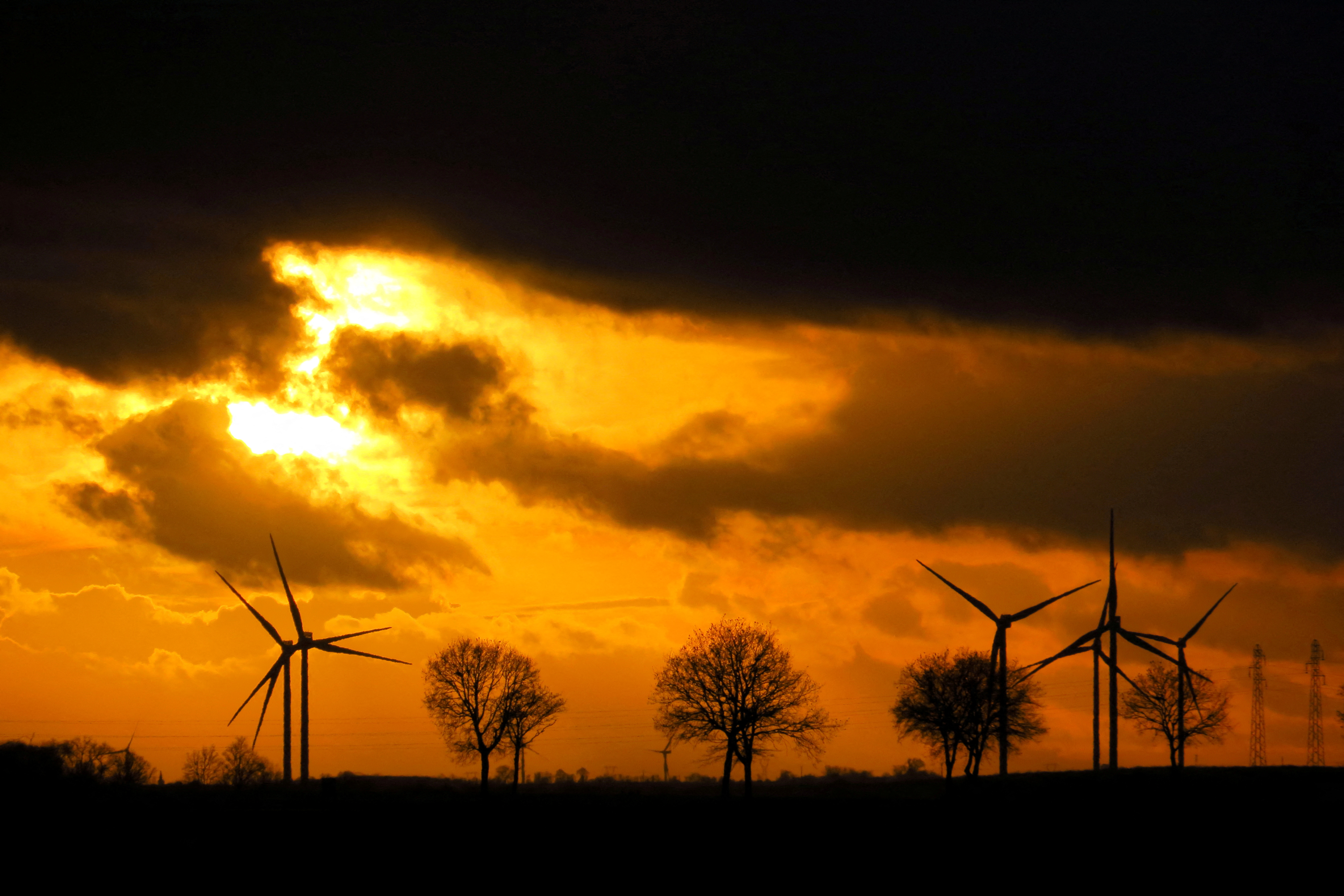 Power-generating windmill turbines and electrical pylons are pictured during sunset at a wind park in Graincourt-les-Havrincourt