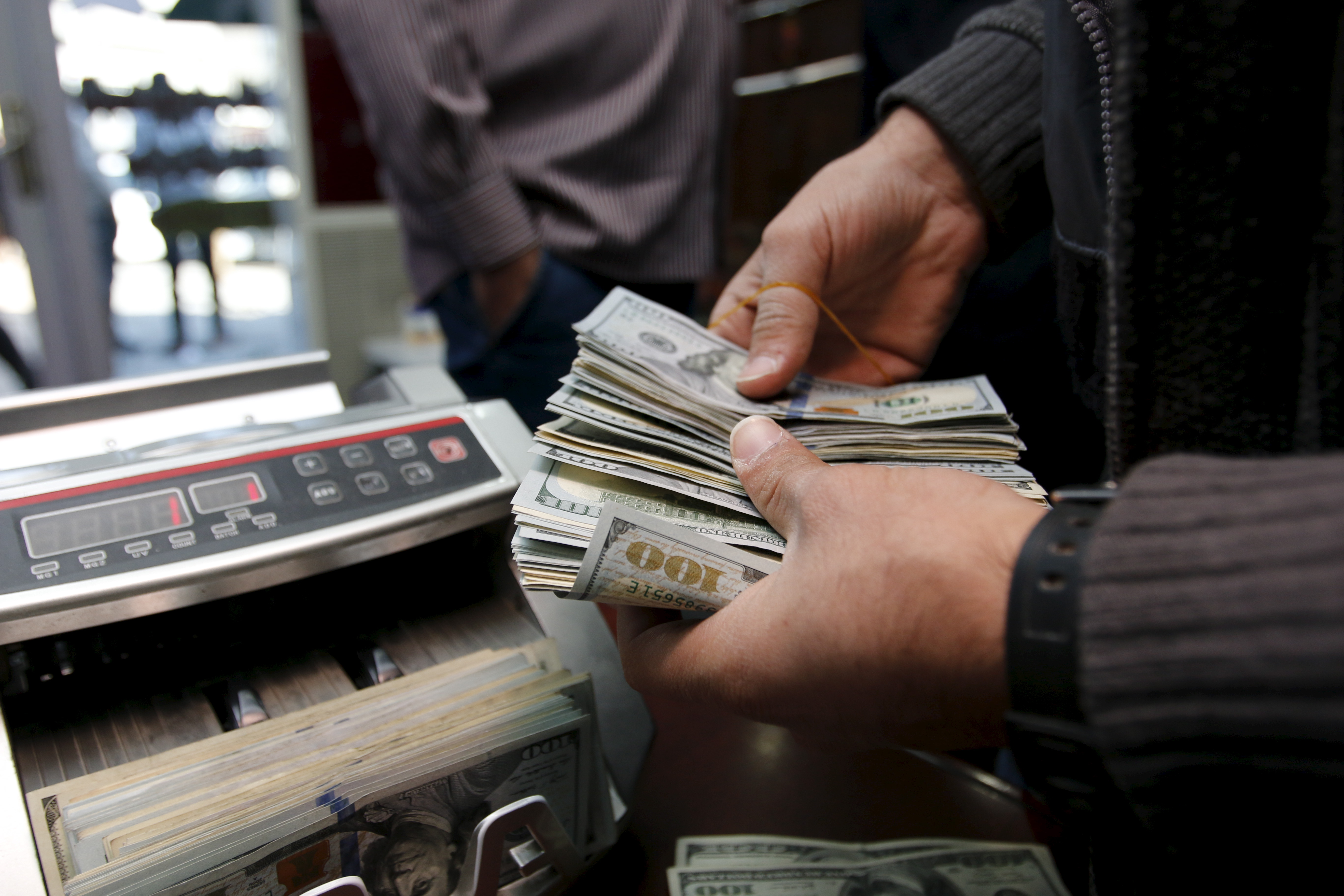 A man counts wads of U.S. dollars on a money counting machine at a currency exchange shop in Baghdad