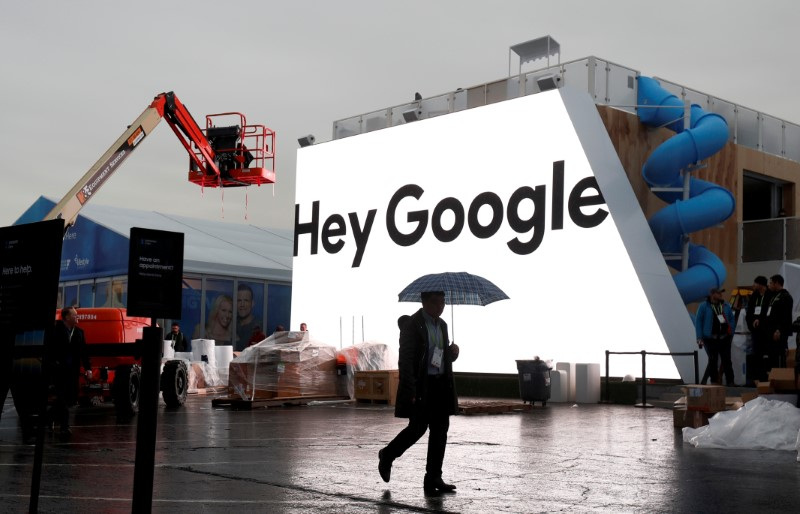 A man walks through light rain in front of the Hey Google booth under construction at the Las Vegas Convention Center in preparation for the 2018 CES in Las Vegas