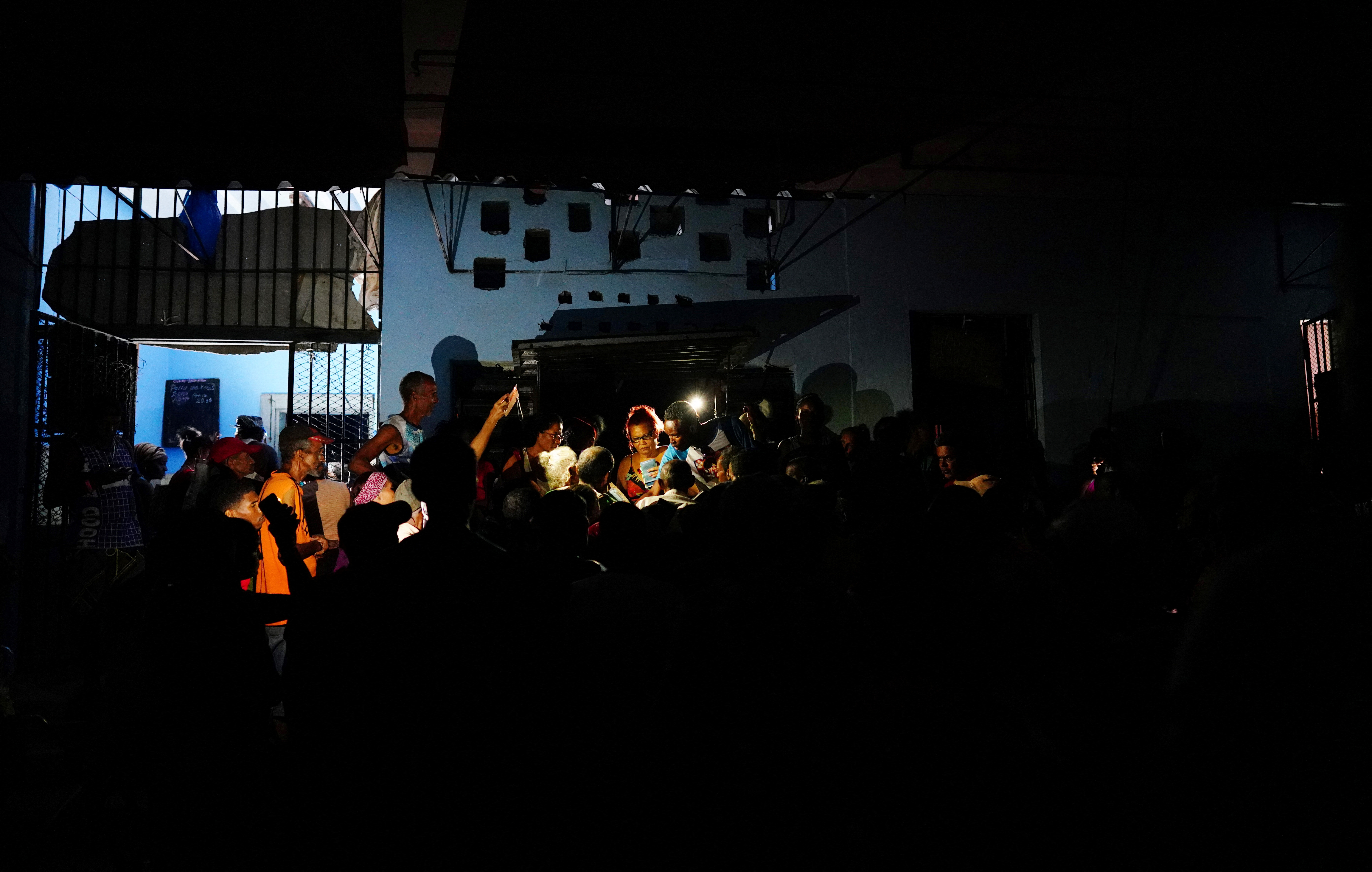 People try to get a once-monthly ration of chicken, during a blackout, at a small state-run market in Santiago