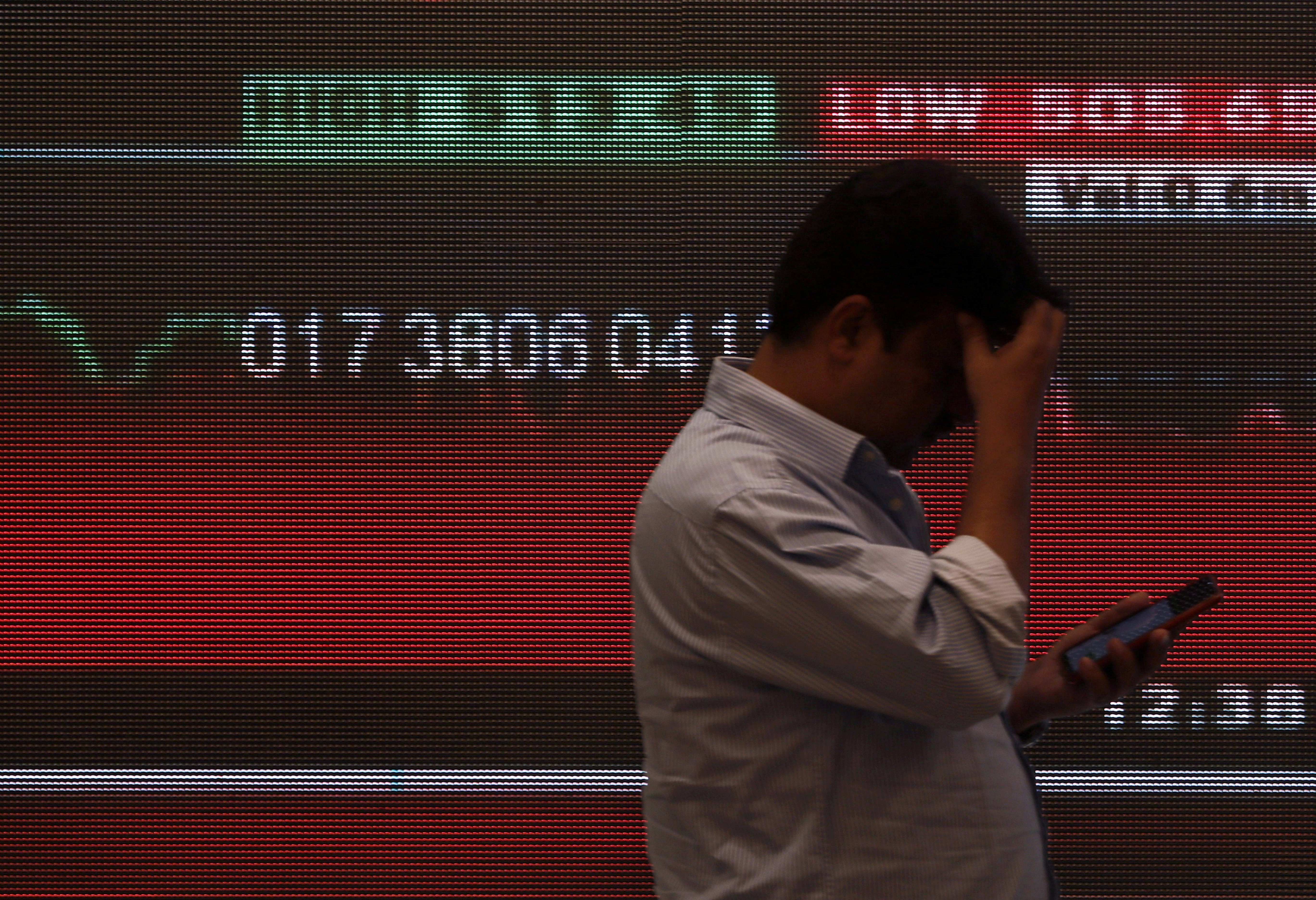 A man stands in front of a screen displaying news of markets updates inside the Bombay Stock Exchange (BSE) building in Mumbai