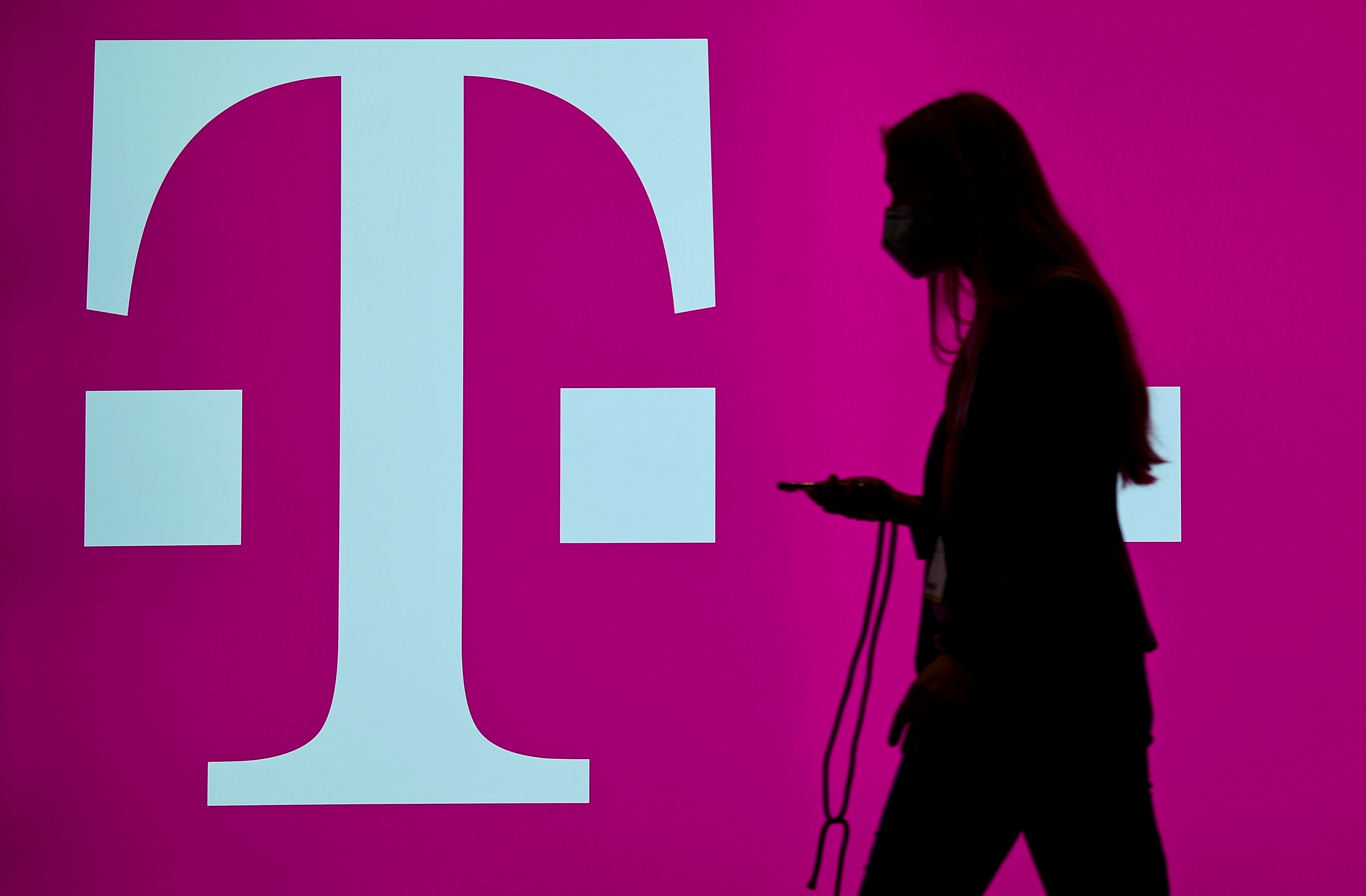 A woman carrying her phone passes by the logo of German telecommunication company 