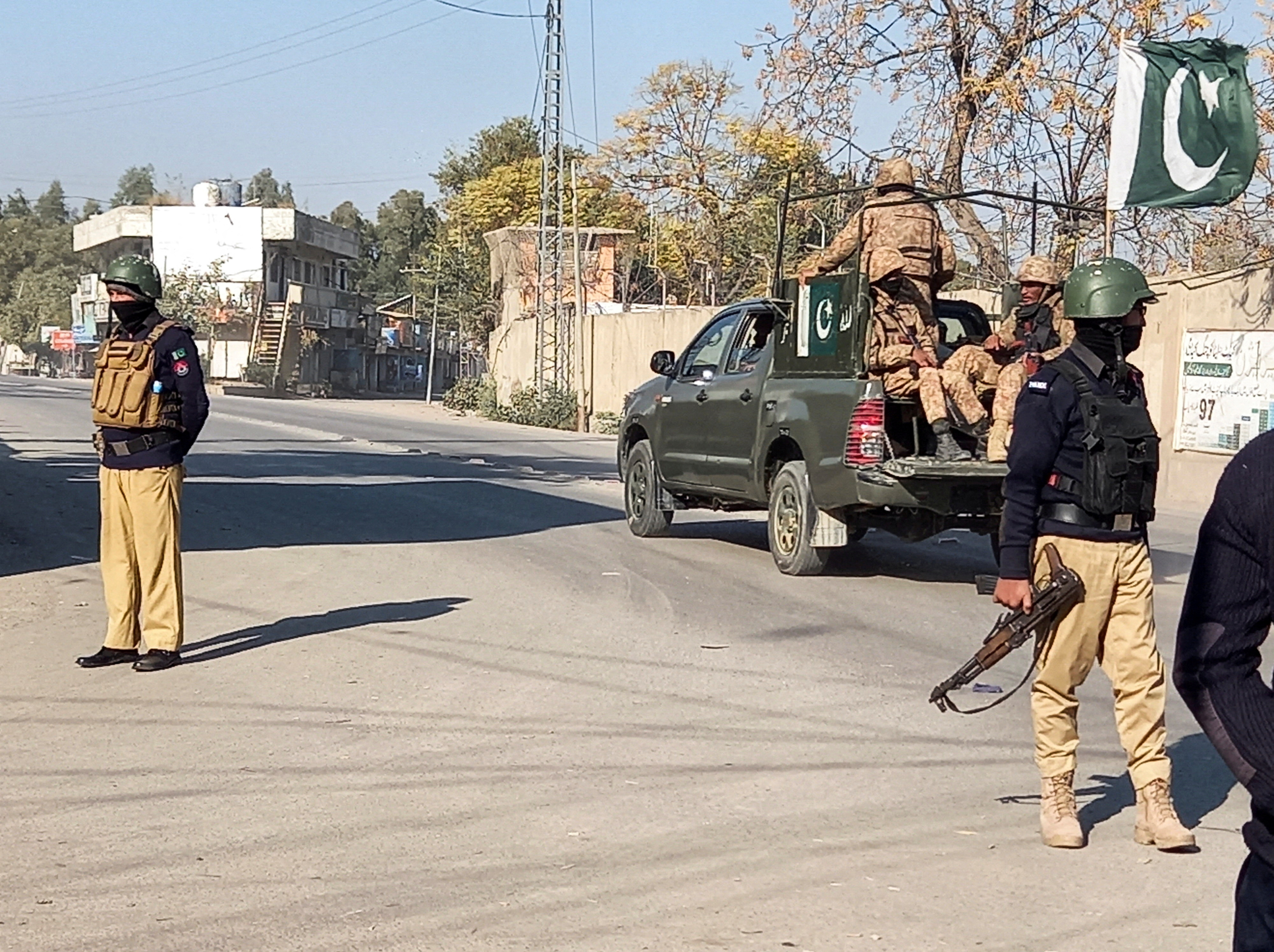 A Pakistani army vehicle patrols past police officers standing guard along a road near a cantonment area in Bannu, Pakistan
